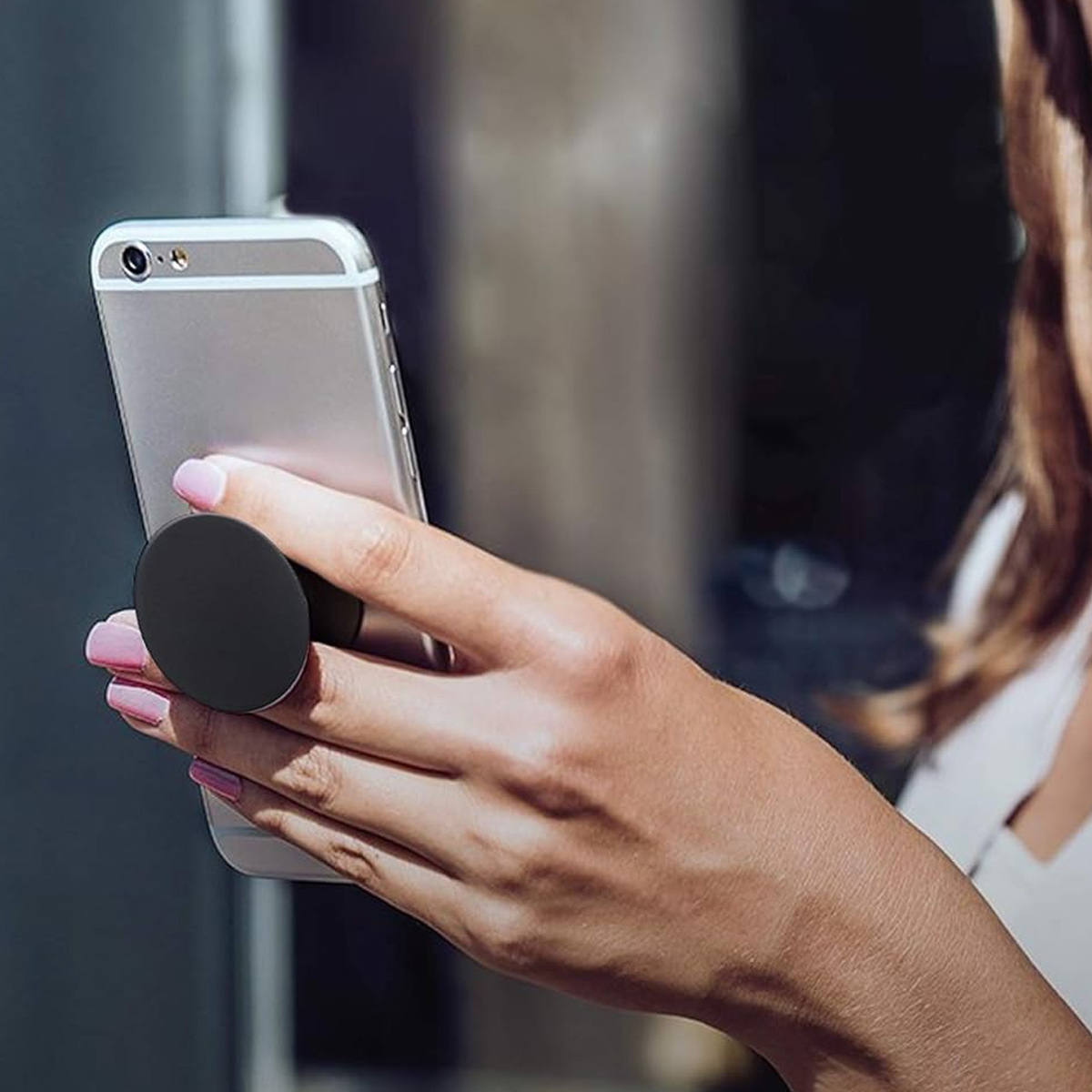 Eine Hand hält ein Telefon mit einem schwarzen Pop-Socket. Das Telefon ist silberfarben, und der Hintergrund ist unscharf.