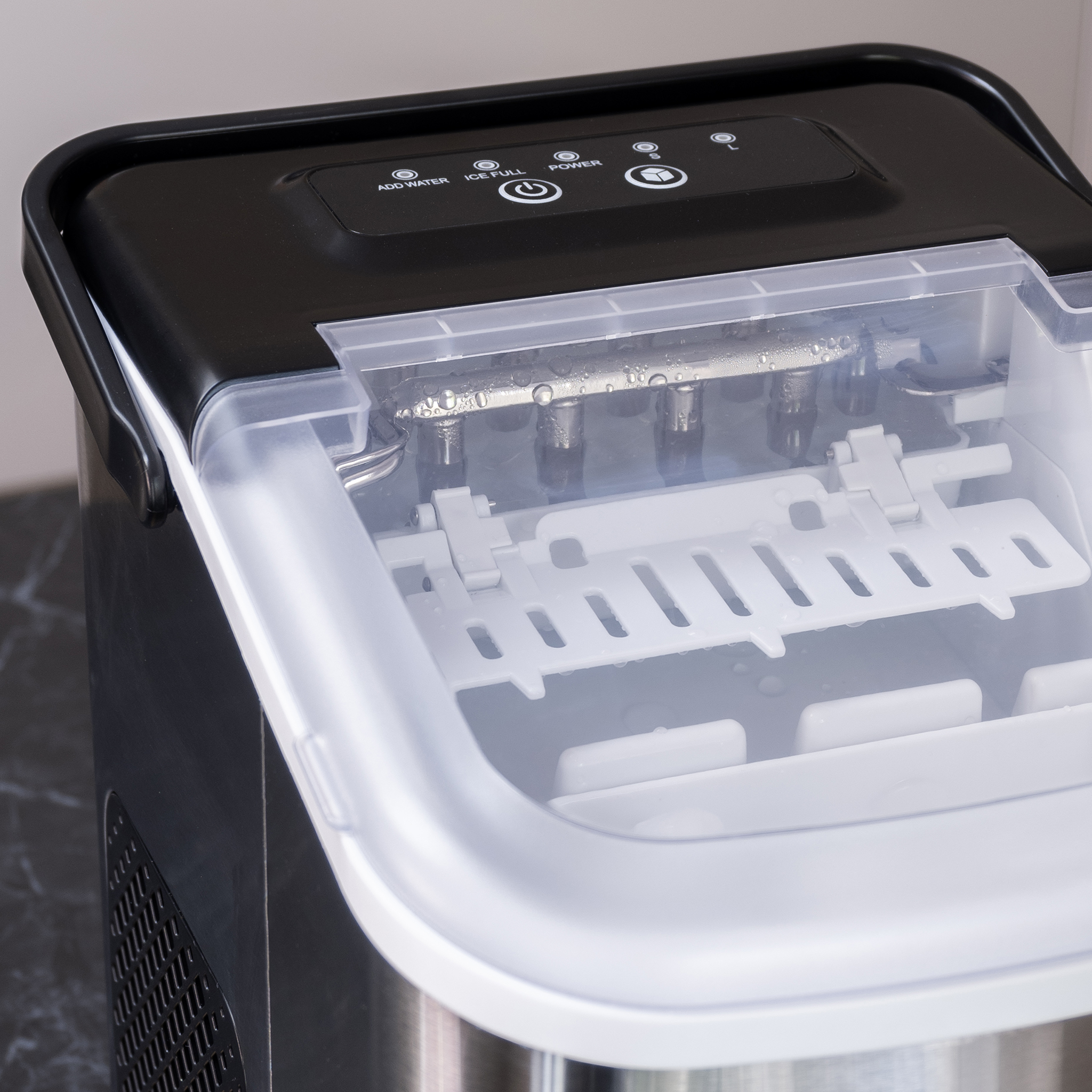 A black and white ice maker machine with an open lid. Ice cubes are inside. The panel has buttons. Close up shot.
