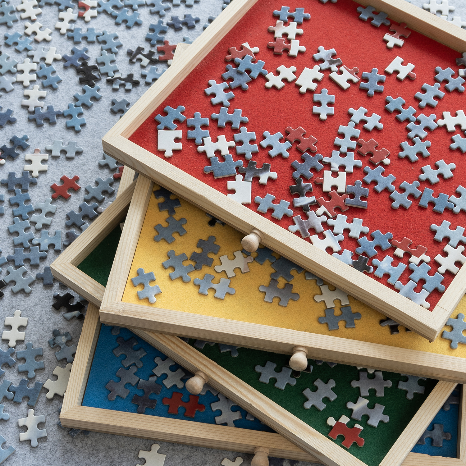 Three trays with puzzle pieces. Each tray has a different color: red, yellow, and blue. A gray surface is visible.