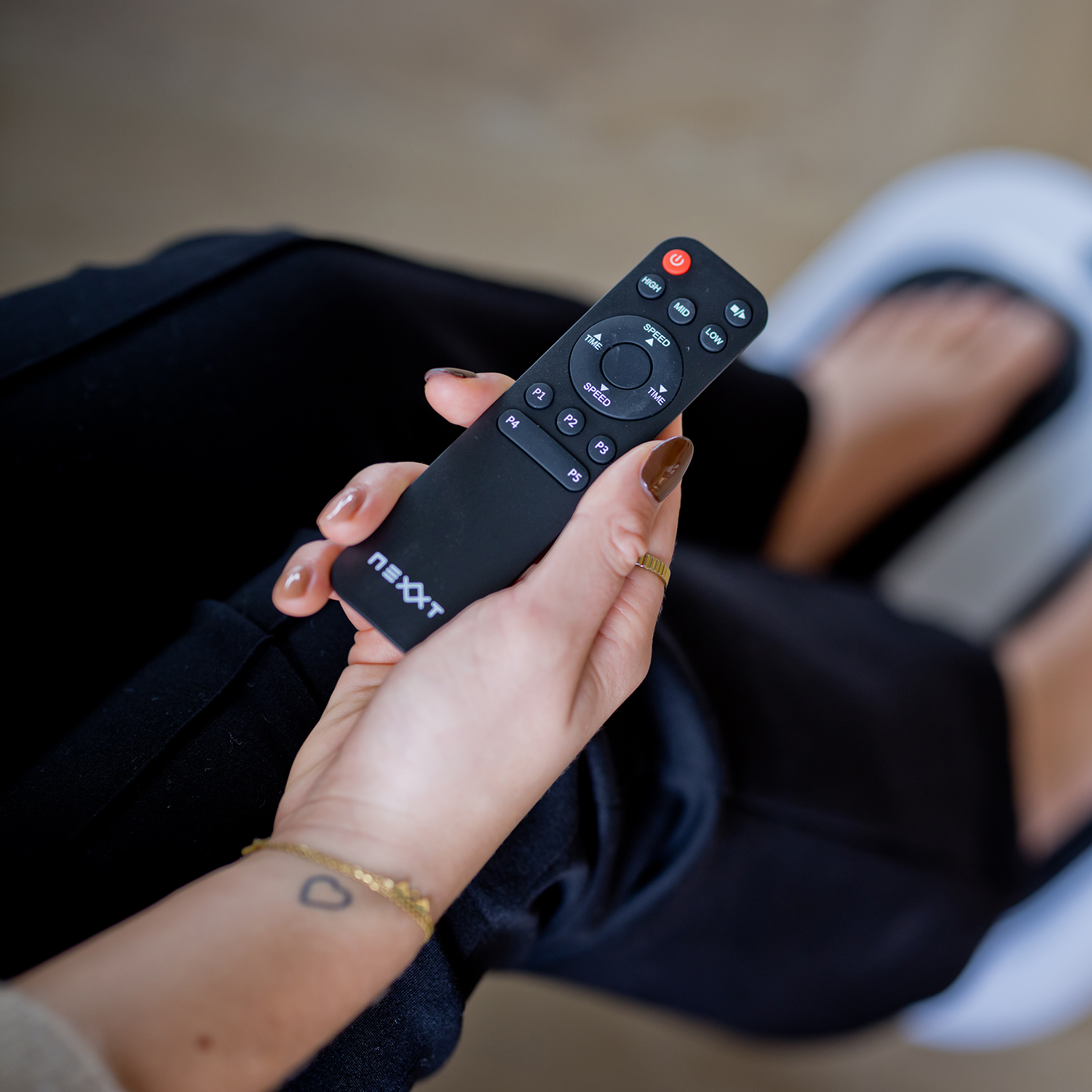 A person's hand holding a black remote control. The remote has multiple buttons and a power button is visible.