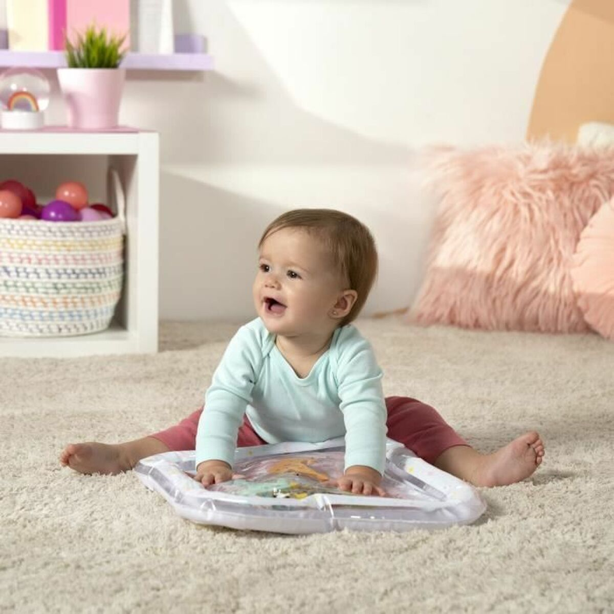 Baby sitzt auf einer Matte und spielt mit Spielzeug. Lächelt. Weißer Hintergrund.