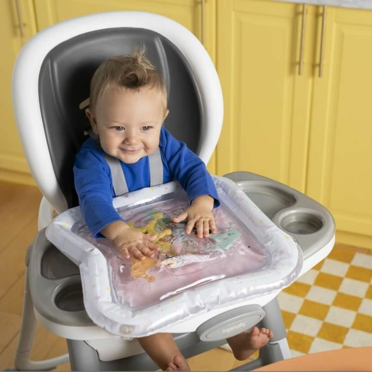 Baby im Hochstuhl spielt mit wassergefüllter Spielmatte.