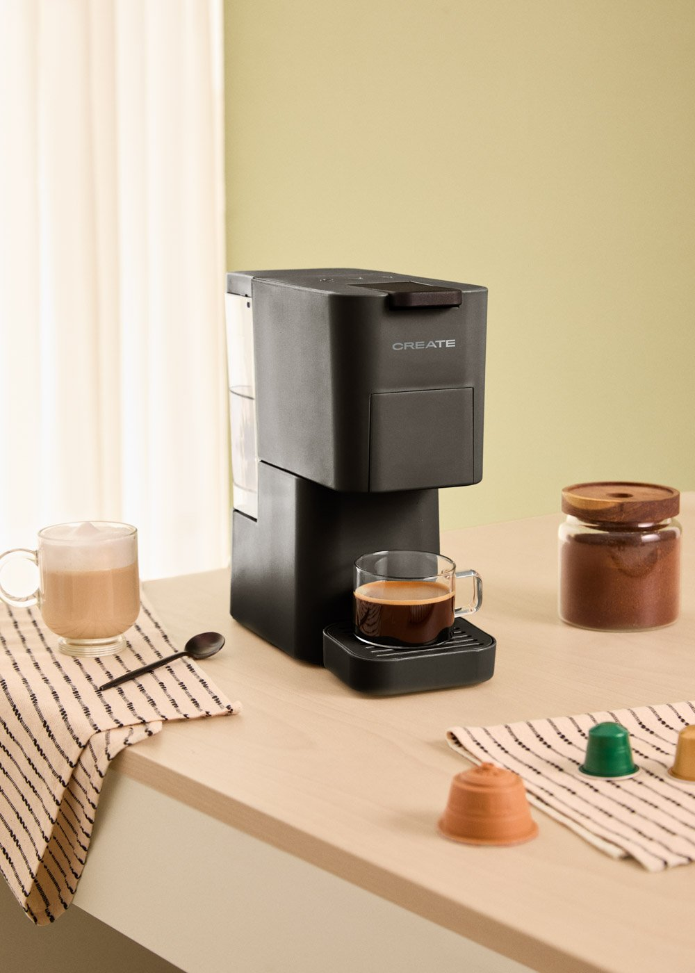 Máquina de espresso negra con taza de café. El café está sobre una superficie de madera clara.