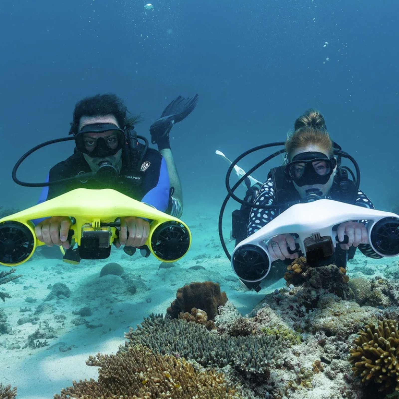Dwóch nurków pływa pod wodą, każdy trzyma żółty i biały skuter podwodny.