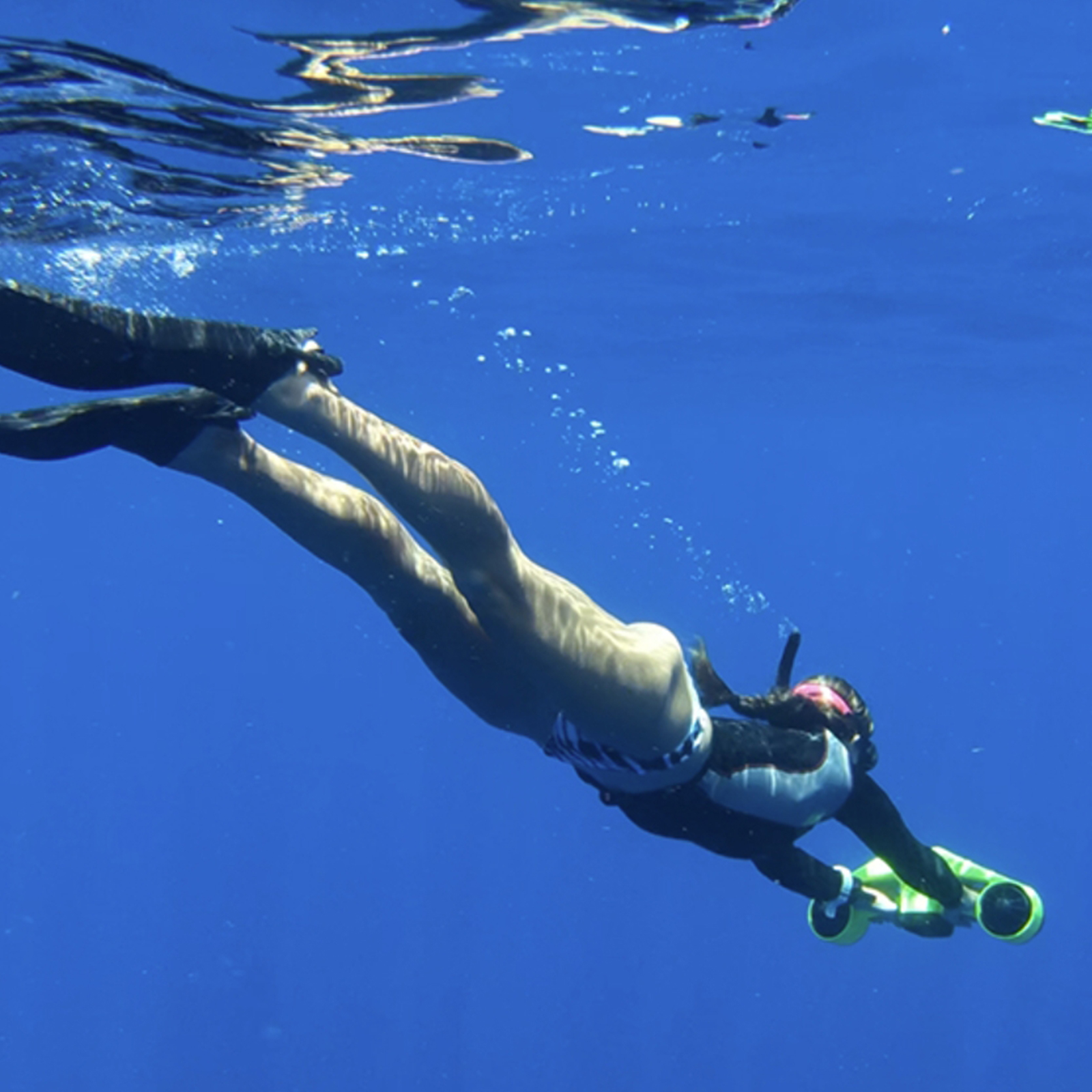 Osoba pod wodą ze skuterem. Osoba ma na sobie płetwy i kombinezon.