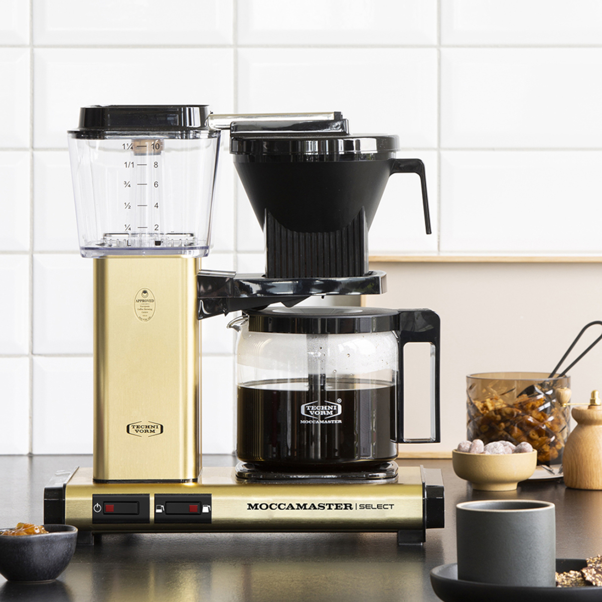 Eine goldene Kaffeemaschine mit Glaskaraffe. Es gibt einen schwarzen Filter und eine Tasse Kaffee.