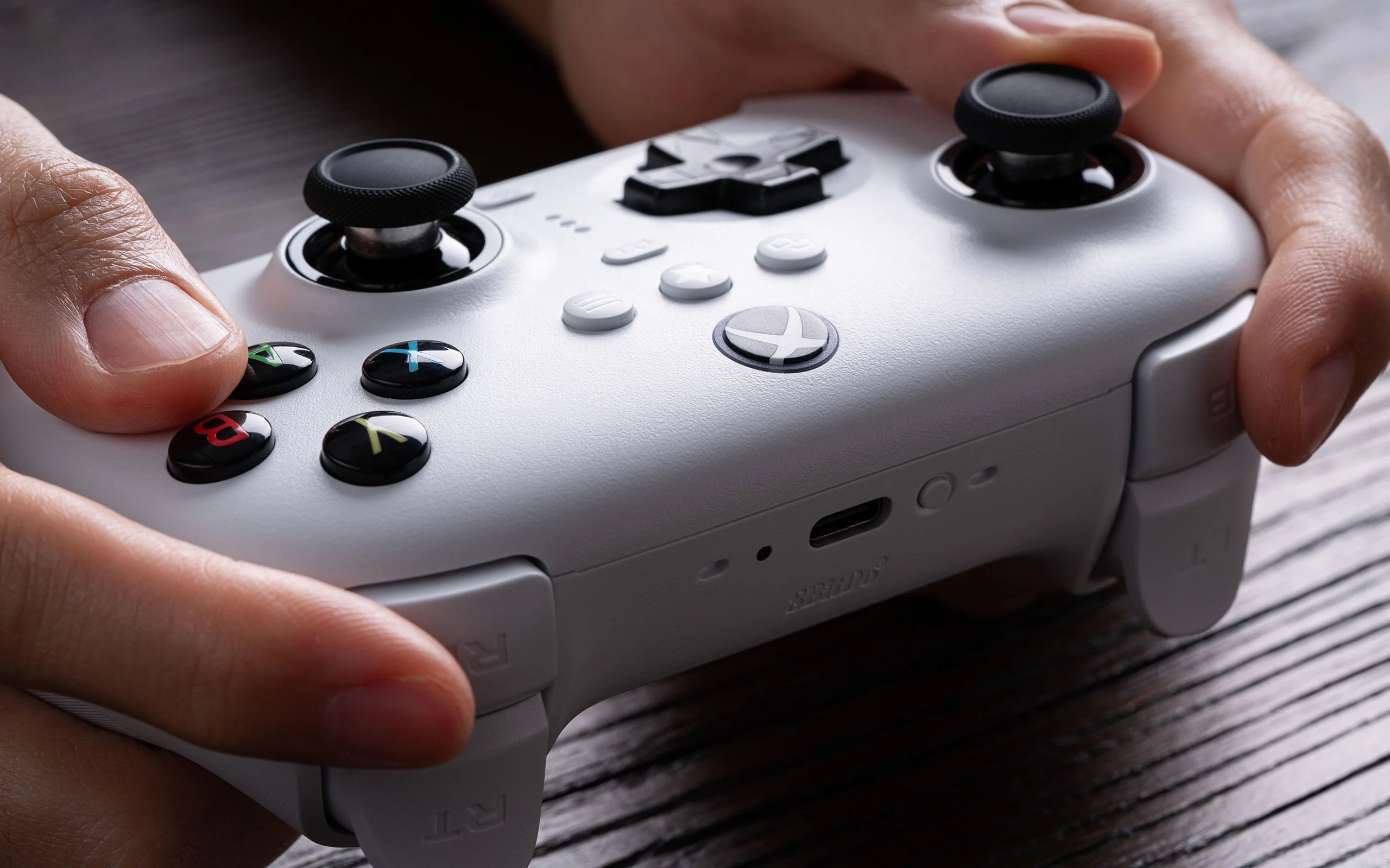 Hände halten einen weißen Gamecontroller, Nahaufnahme. Die Knöpfe sind schwarz und bunt.