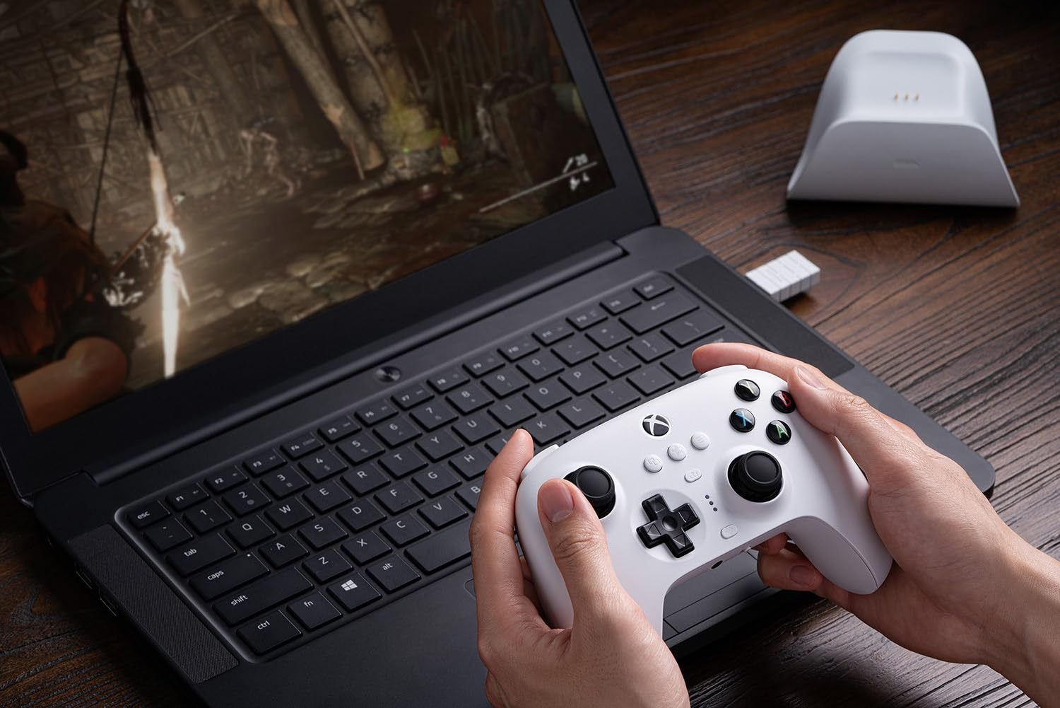 Hände halten einen weißen Controller und spielen ein Spiel auf einem Laptop.