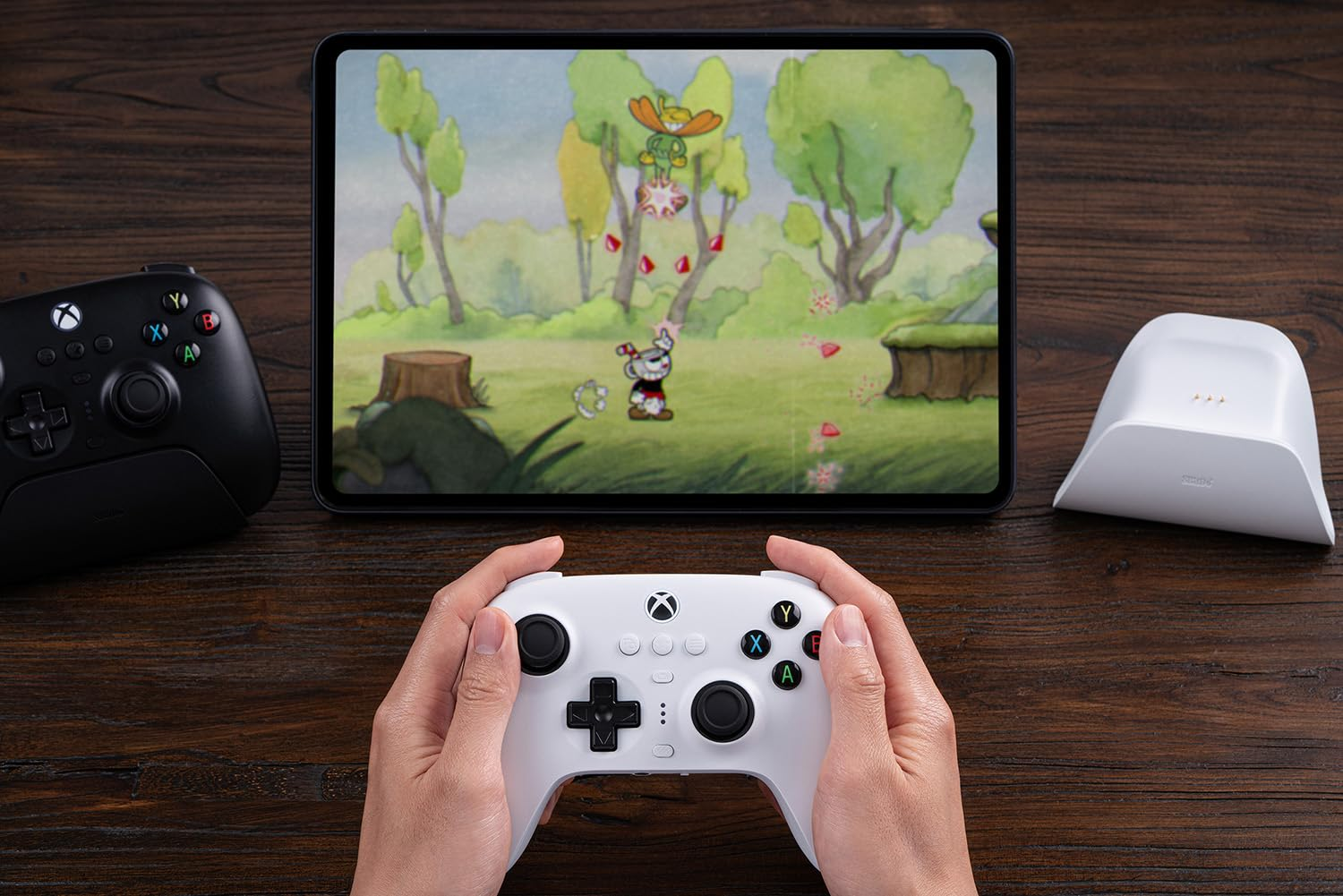 Hände halten einen weißen Controller und spielen ein Spiel auf einem Tablet.