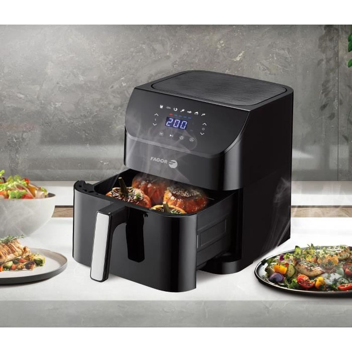 Eine schwarze Heißluftfritteuse mit geöffneter Schublade, die gekochtes Essen zeigt. Es steht auf einer Theke mit anderen Gerichten in der Nähe.