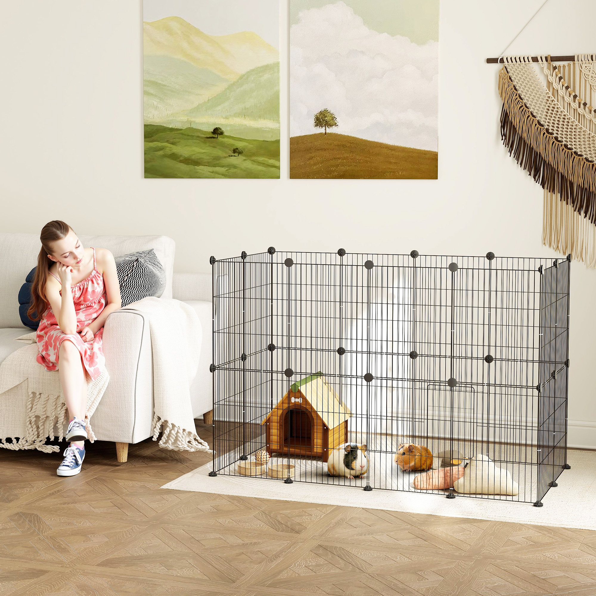 Eine Frau sitzt neben einem Sofa und betrachtet Meerschweinchen in einem schwarzen Gehege. Das Gehege hat ein Haus.