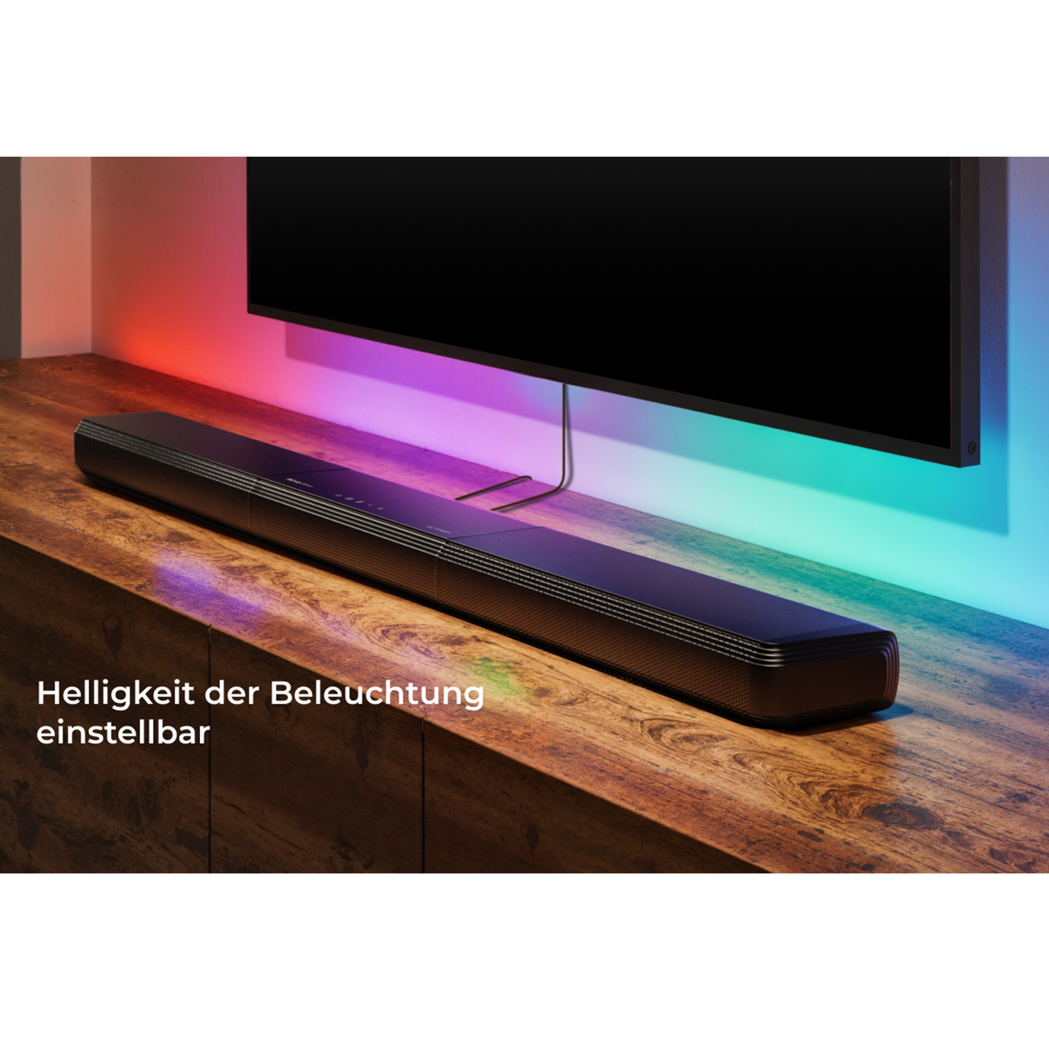 Eine schwarze Soundbar auf einem Holzschrank. Ein großer Fernseher ist darüber. Mehrfarbige Lichter.