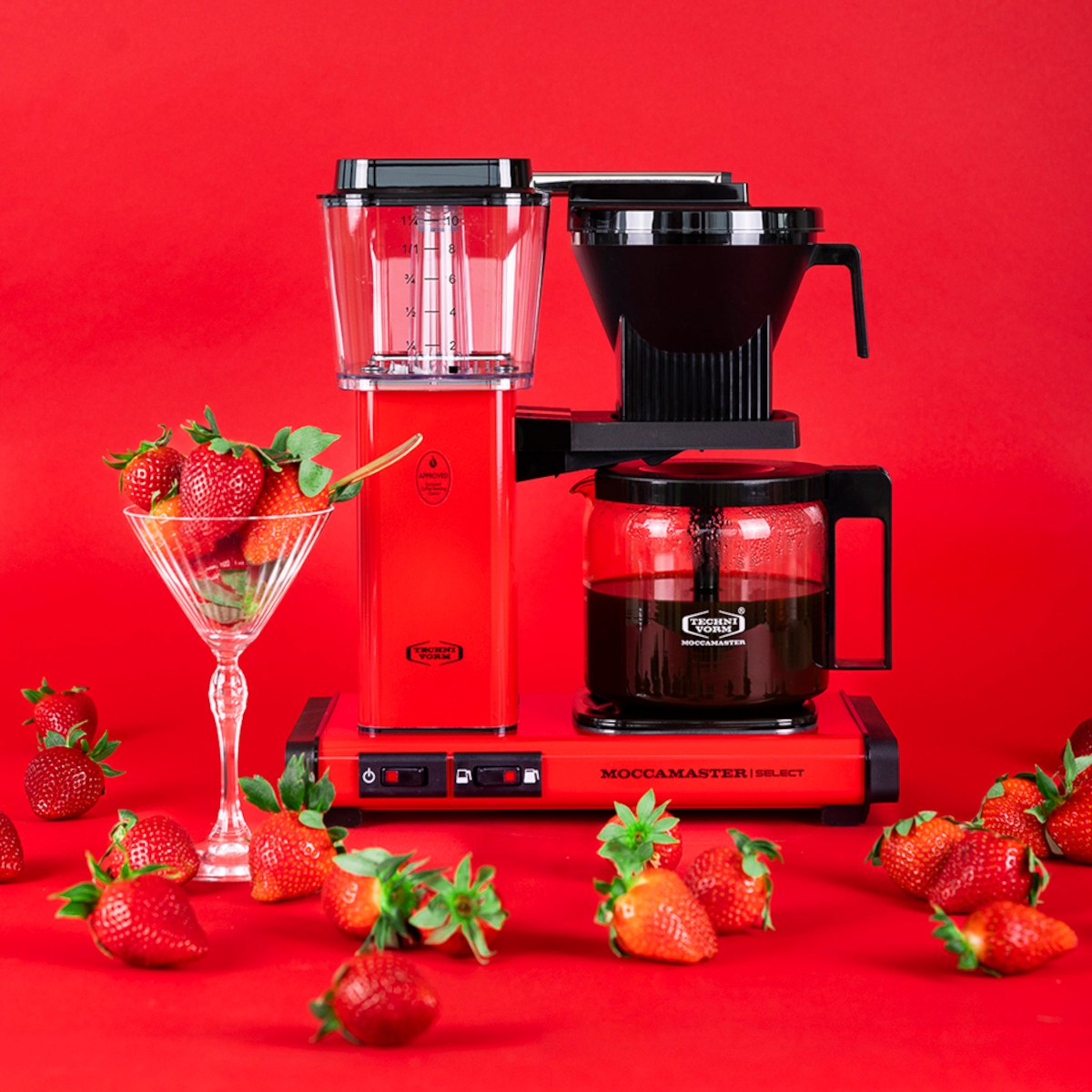 Czerwony ekspres do kawy z truskawkami w kieliszku do martini. Czerwone tło. Truskawki są rozrzucone po scenie.