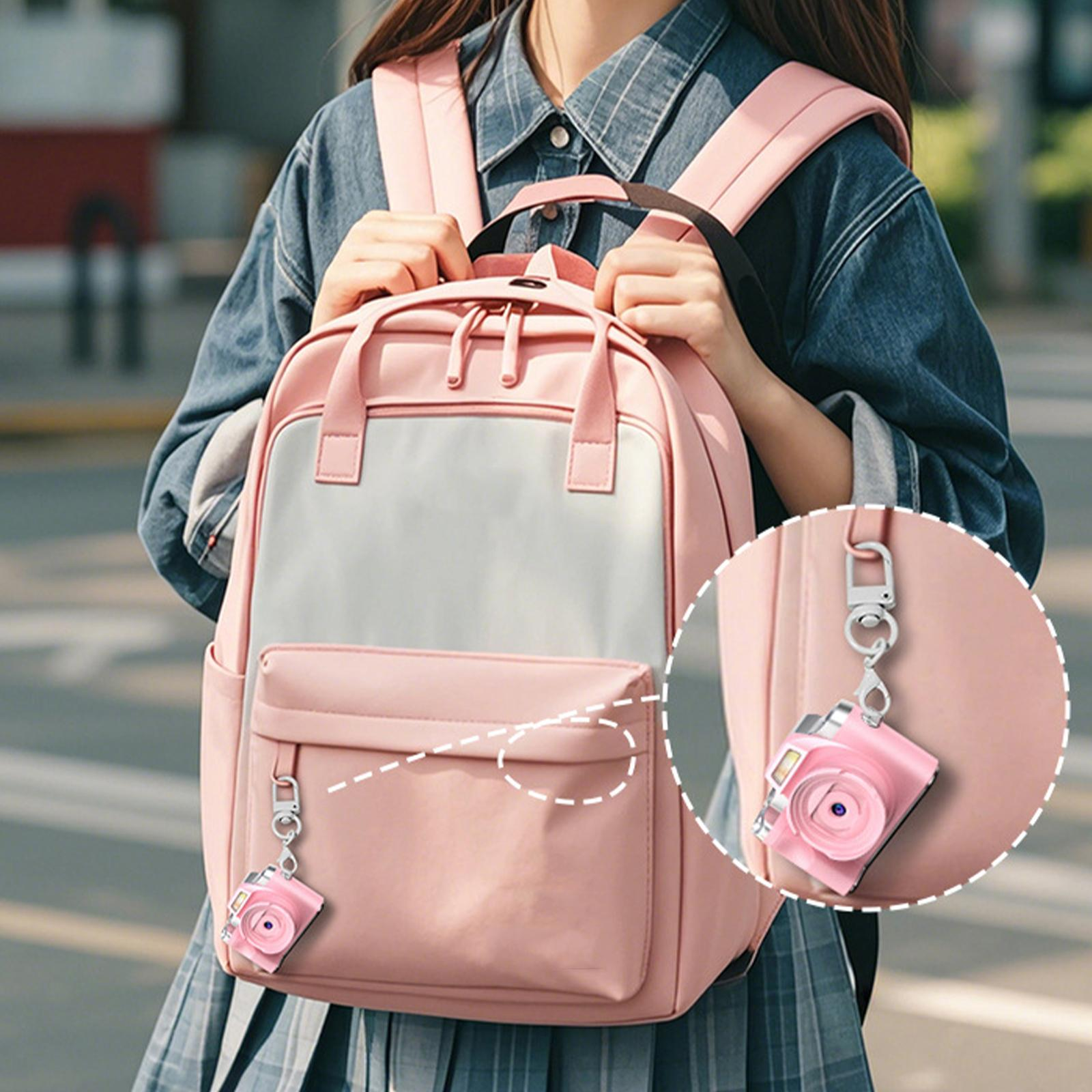 Ein rosa Rucksack mit kleinem Kamera-Schlüsselanhänger, gehalten von einer Person in Jeanshemd.
