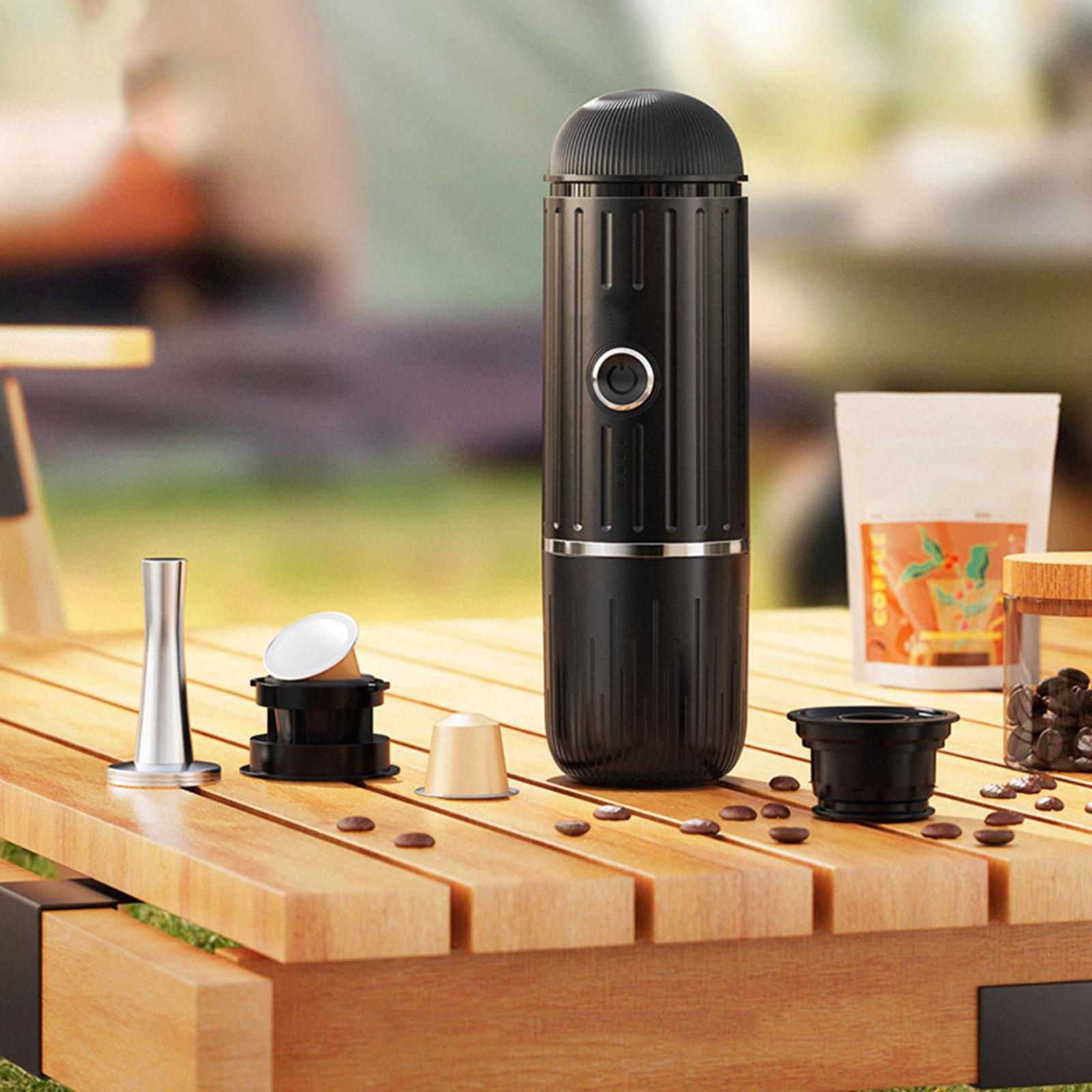 Schwarze tragbare Espressomaschine auf einem Holztisch mit Kaffeebohnen und Zubehör.