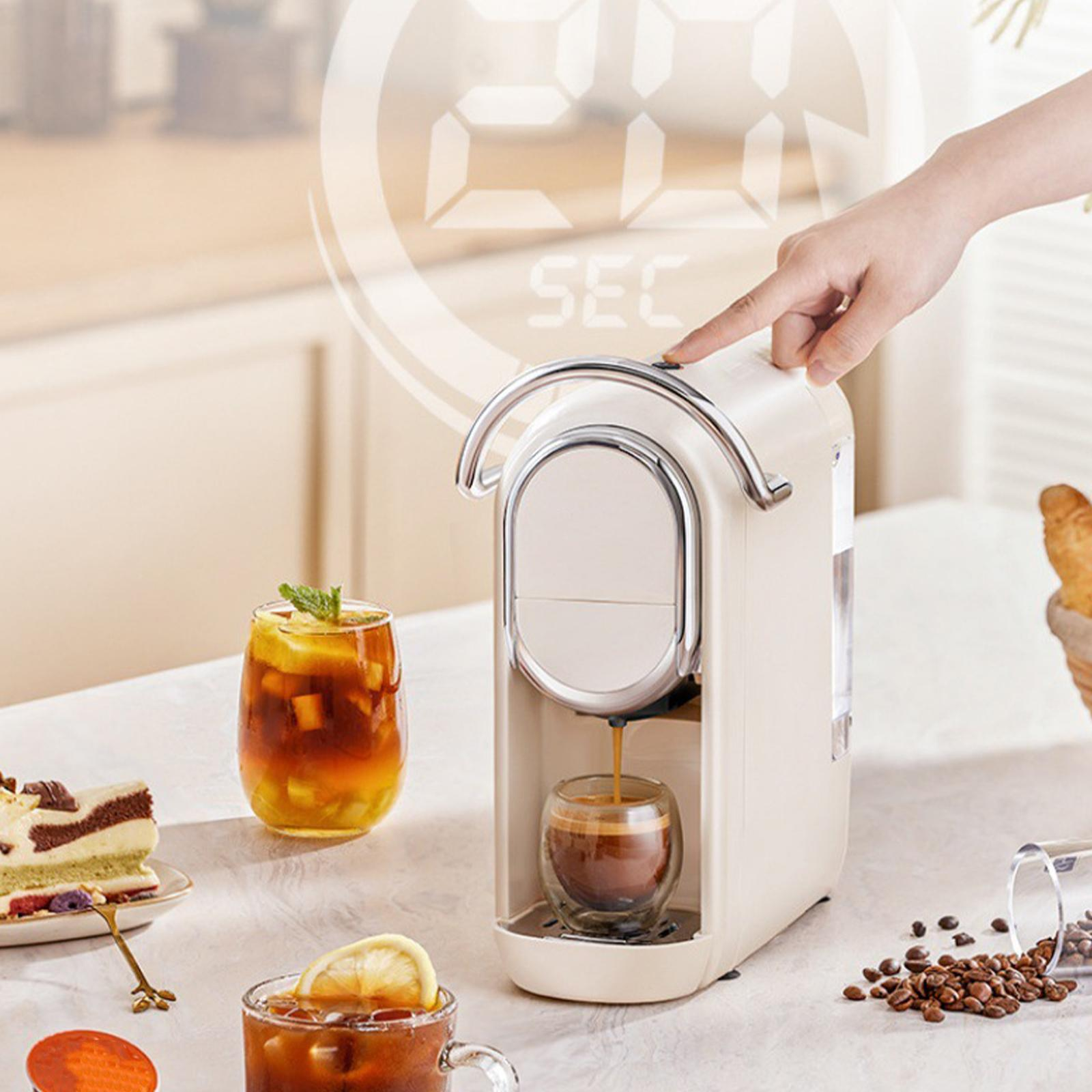 Eine Kaffeemaschine gießt Kaffee in ein Glas. Die Hand einer Person drückt den Knopf. Kaffeepads sind in der Nähe.