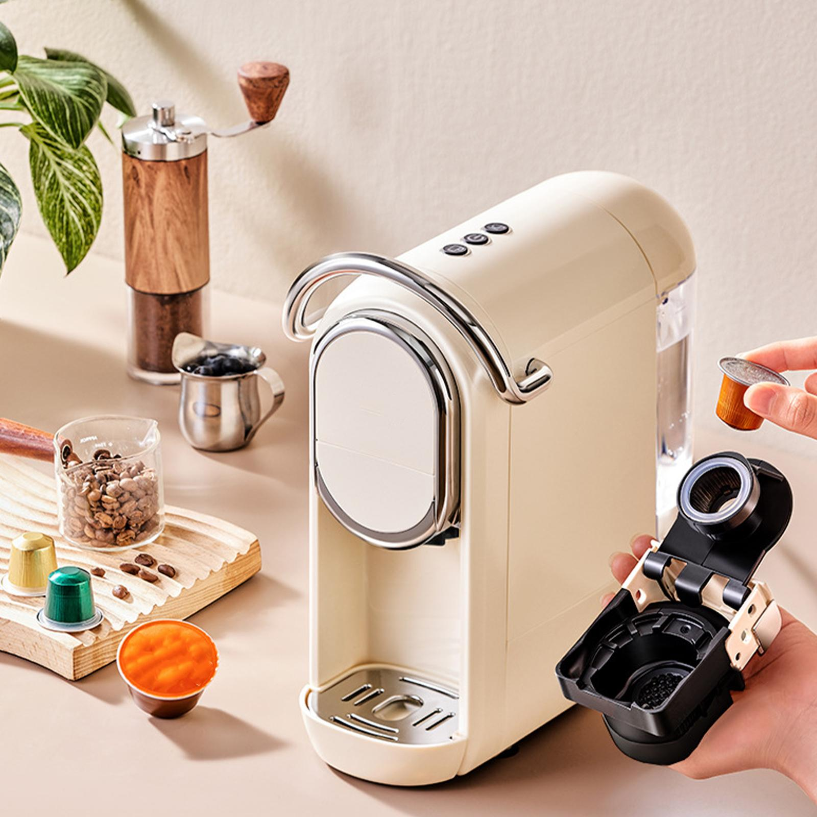 Eine elfenbeinfarbene Espressomaschine mit Chromgriff, eine Hand, die eine Kaffeekapsel hinzufügt, und anderes Kaffeezubehör.