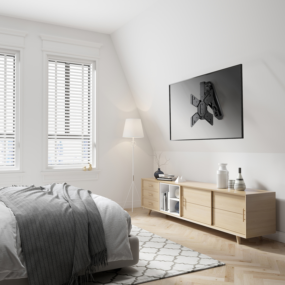 Ein Fernseher ist an einer weißen Wand montiert. Darunter ein Holzschrank und ein Bett mit grauer Decke.
