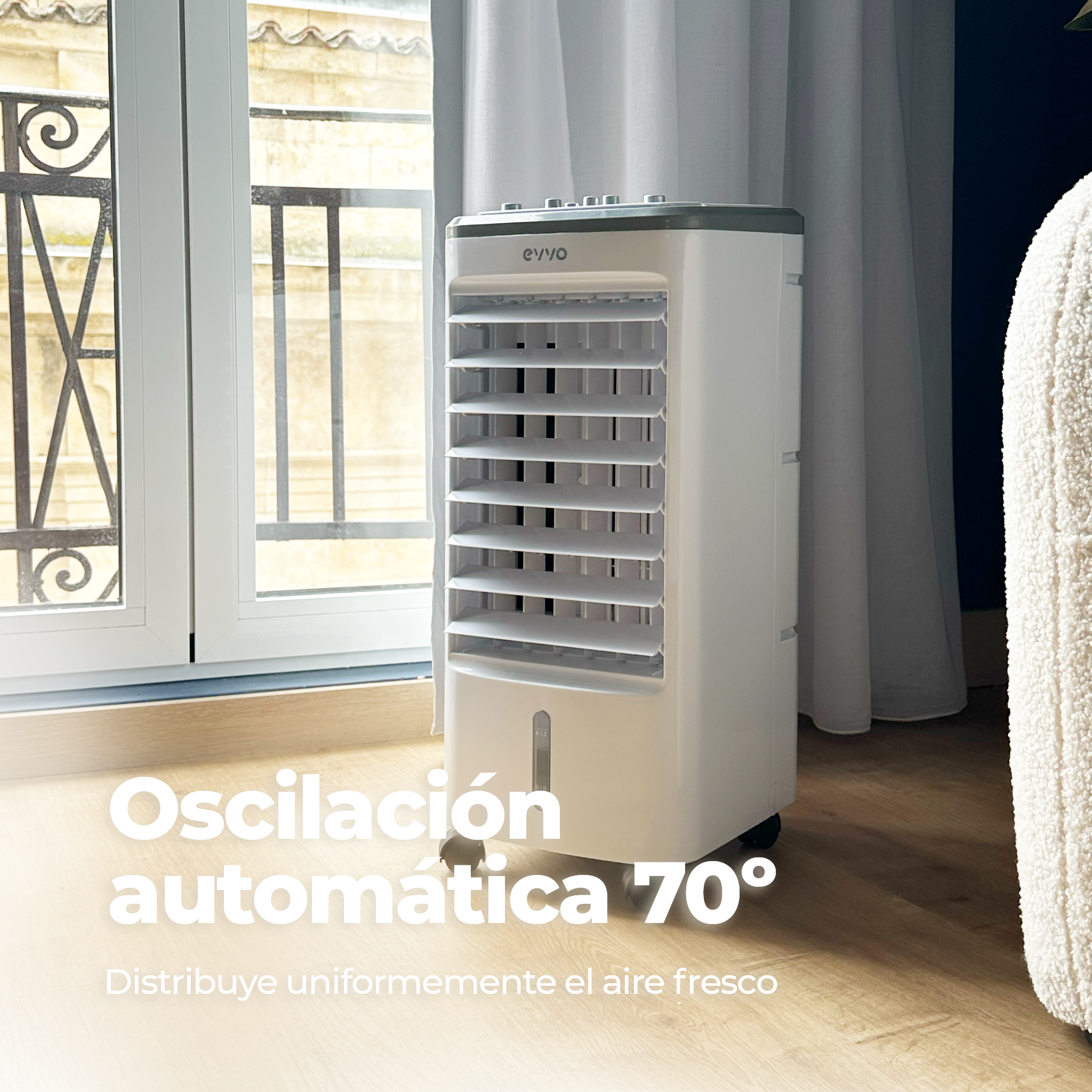 Un enfriador de aire blanco con texto 'Oscilación automática 70°', cerca de una ventana y un sofá blanco.