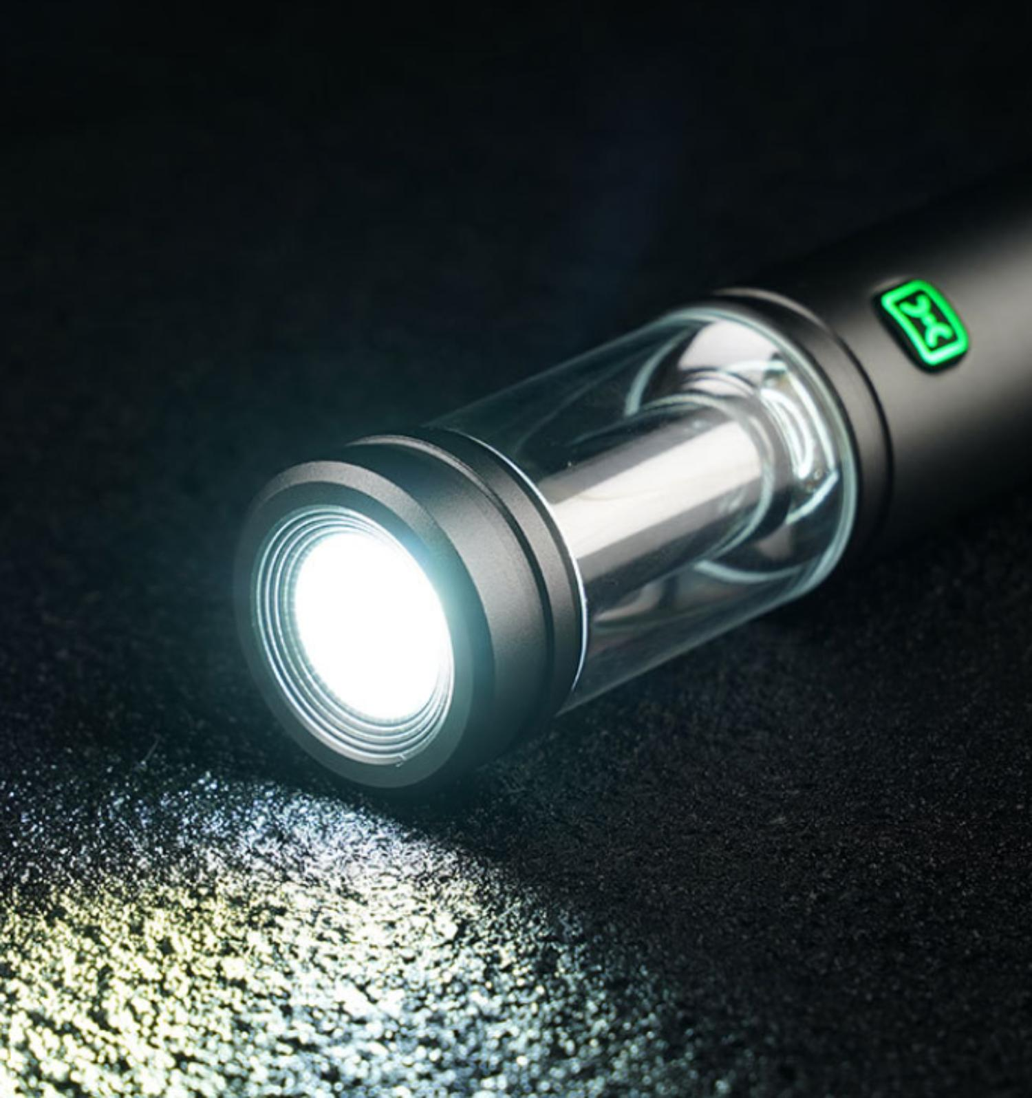 Ein schwarzer Vape-Pen mit einem leuchtenden weißen Licht, das vom Ende ausgeht und auf eine dunkle Oberfläche scheint.
