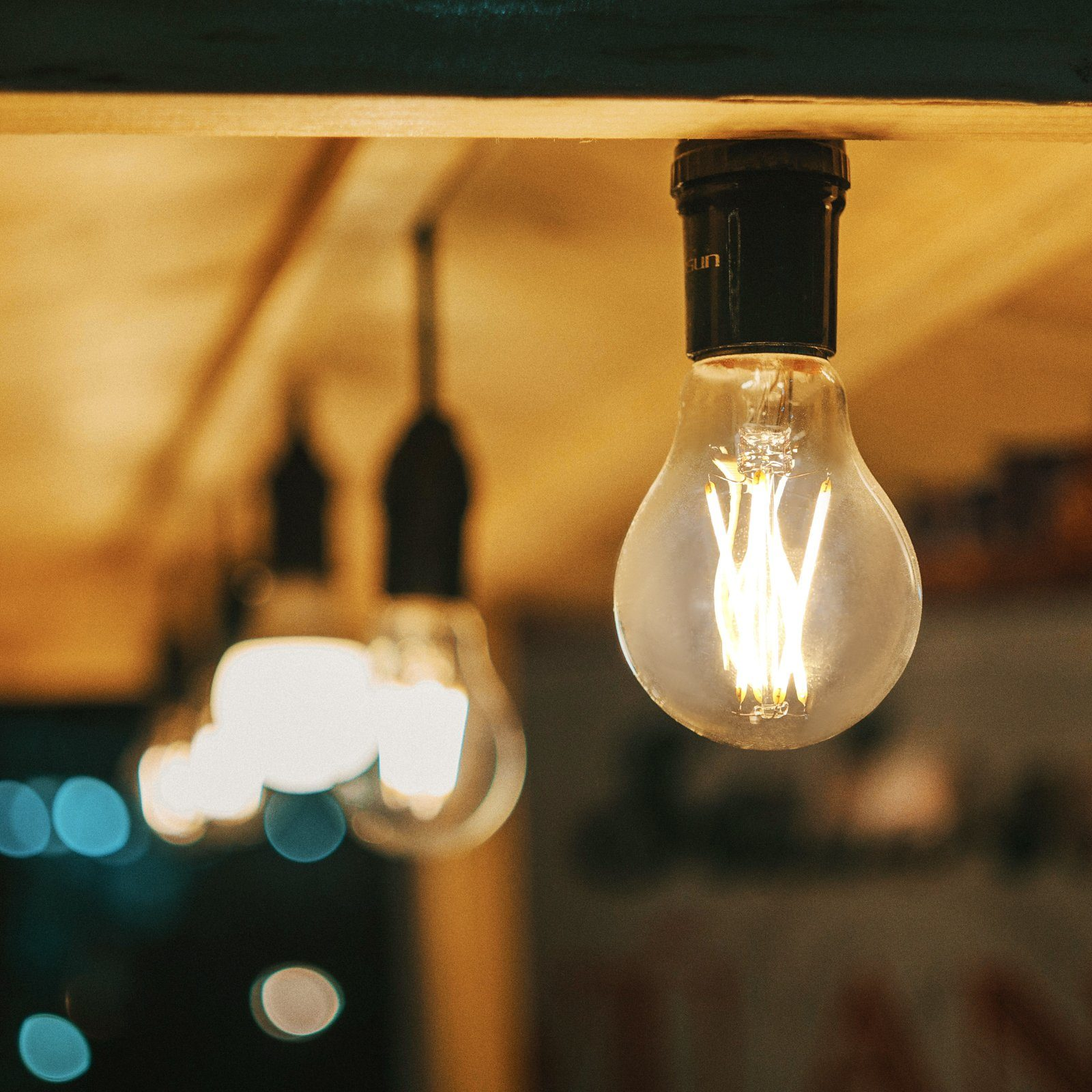 Kilka zapalonych żarówek zwisających z sufitu. Żarówka na pierwszym planie jest ostra i wyraźna.