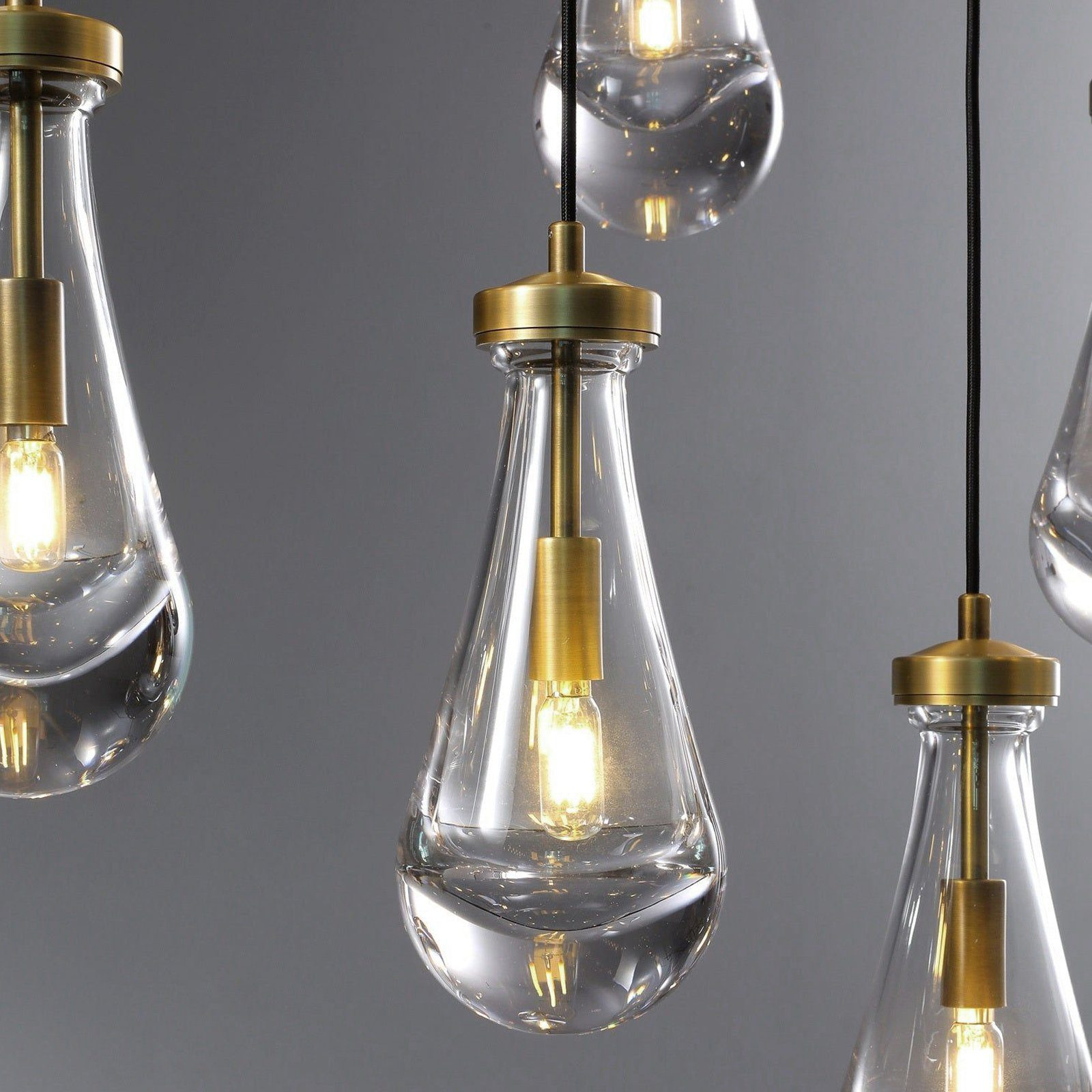 Pięć żarówek w kształcie łzy. Każda ma przezroczysty szklany wygląd i mosiężny wierzch. Światła są włączone.