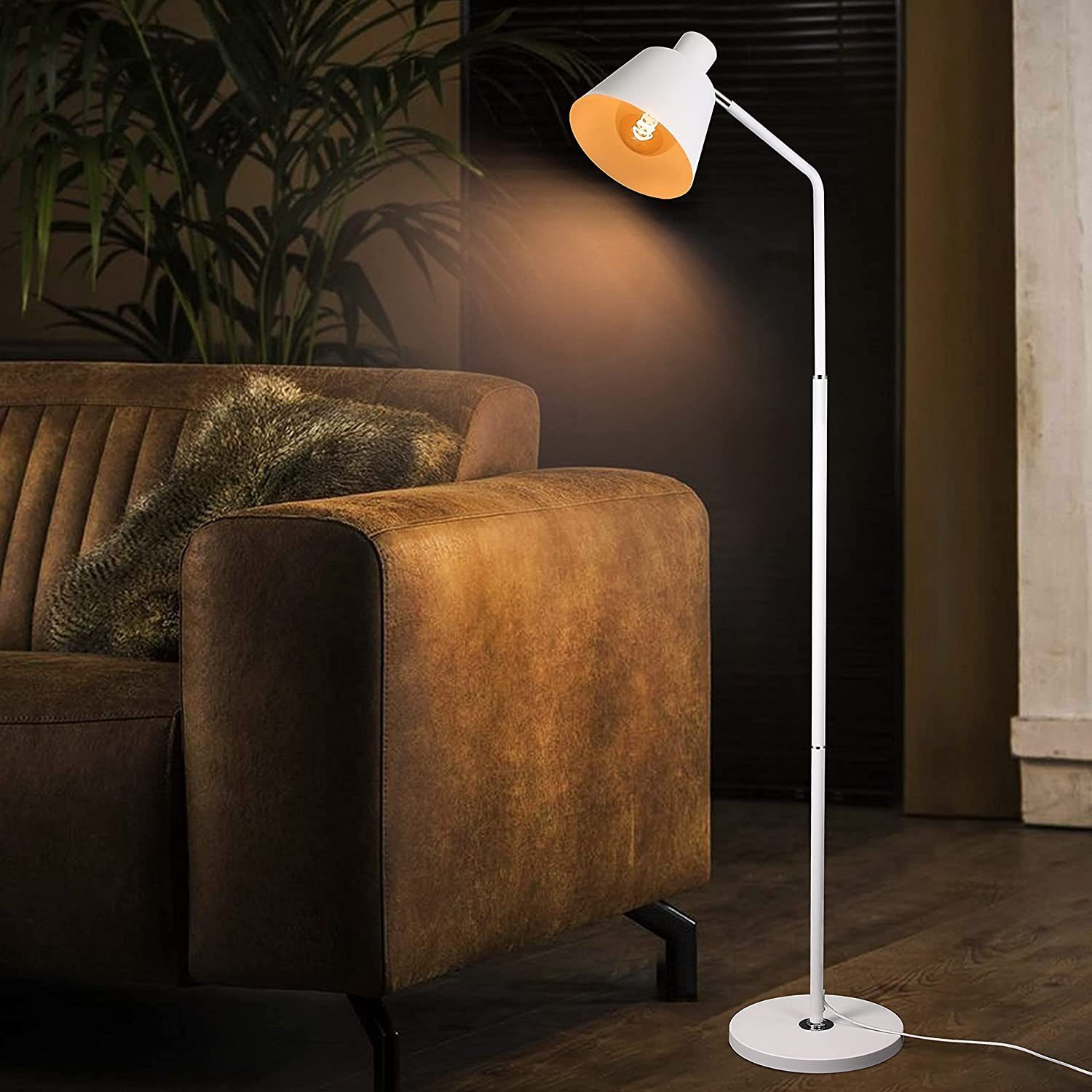 Eine weiße Stehlampe mit einem weißen Lampenschirm. Im Hintergrund ein braunes Sofa. Das Licht ist an.