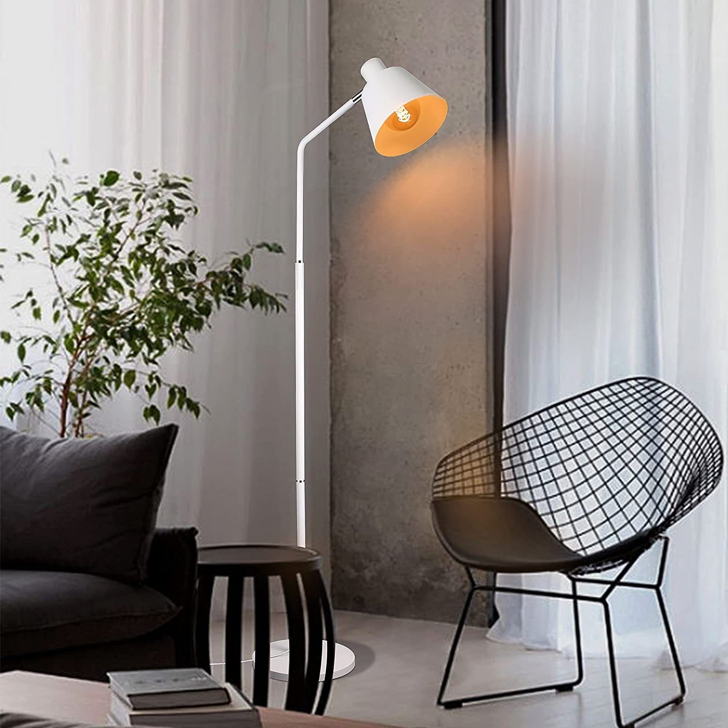 Eine weiße Stehlampe mit weißem Lampenschirm und einem schwarzen Stuhl, neben einer Pflanze und einem schwarzen Hocker.