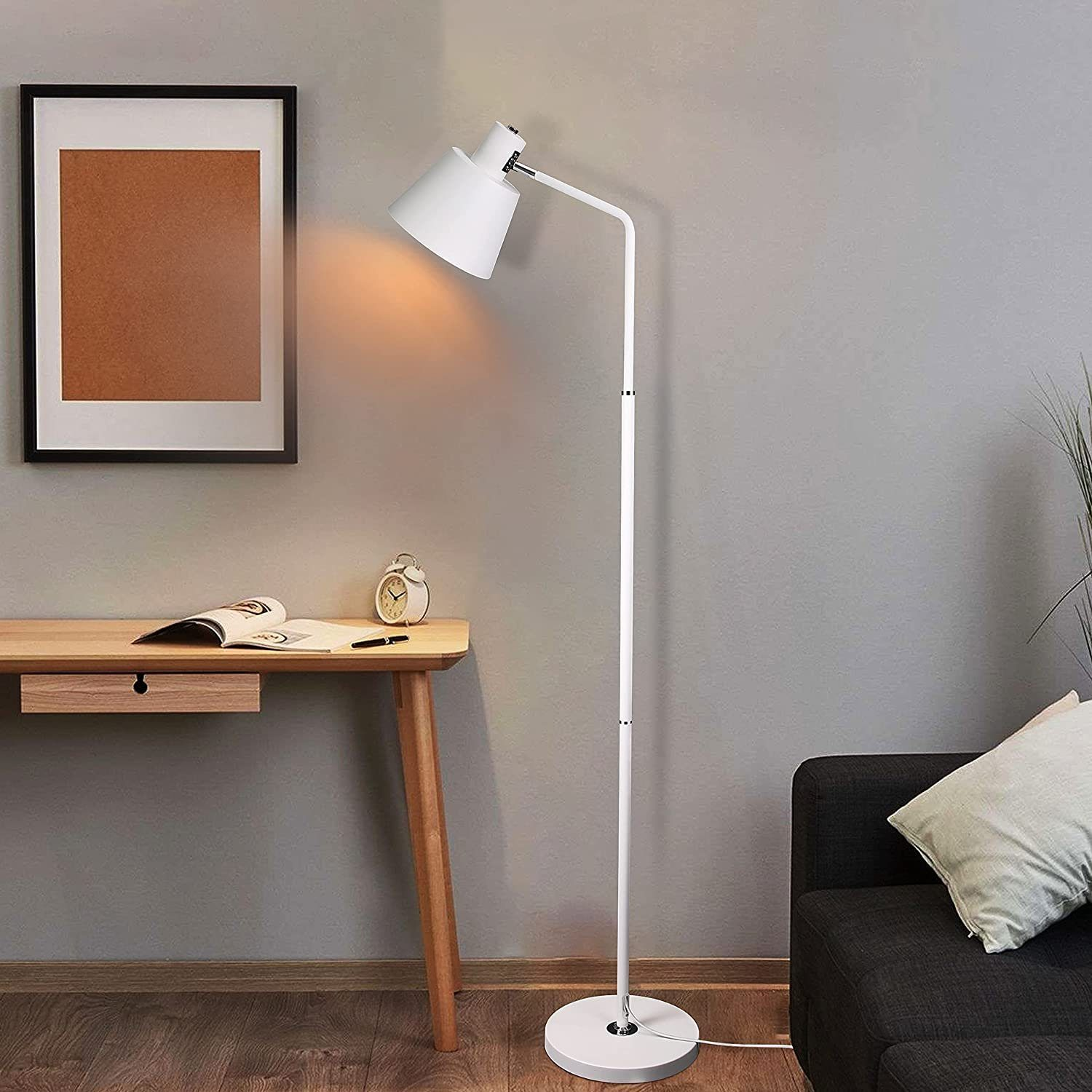Eine weiße Stehlampe mit weißem Lampenschirm, neben einem Schreibtisch, Stuhl und einem Gemälde an der Wand.
