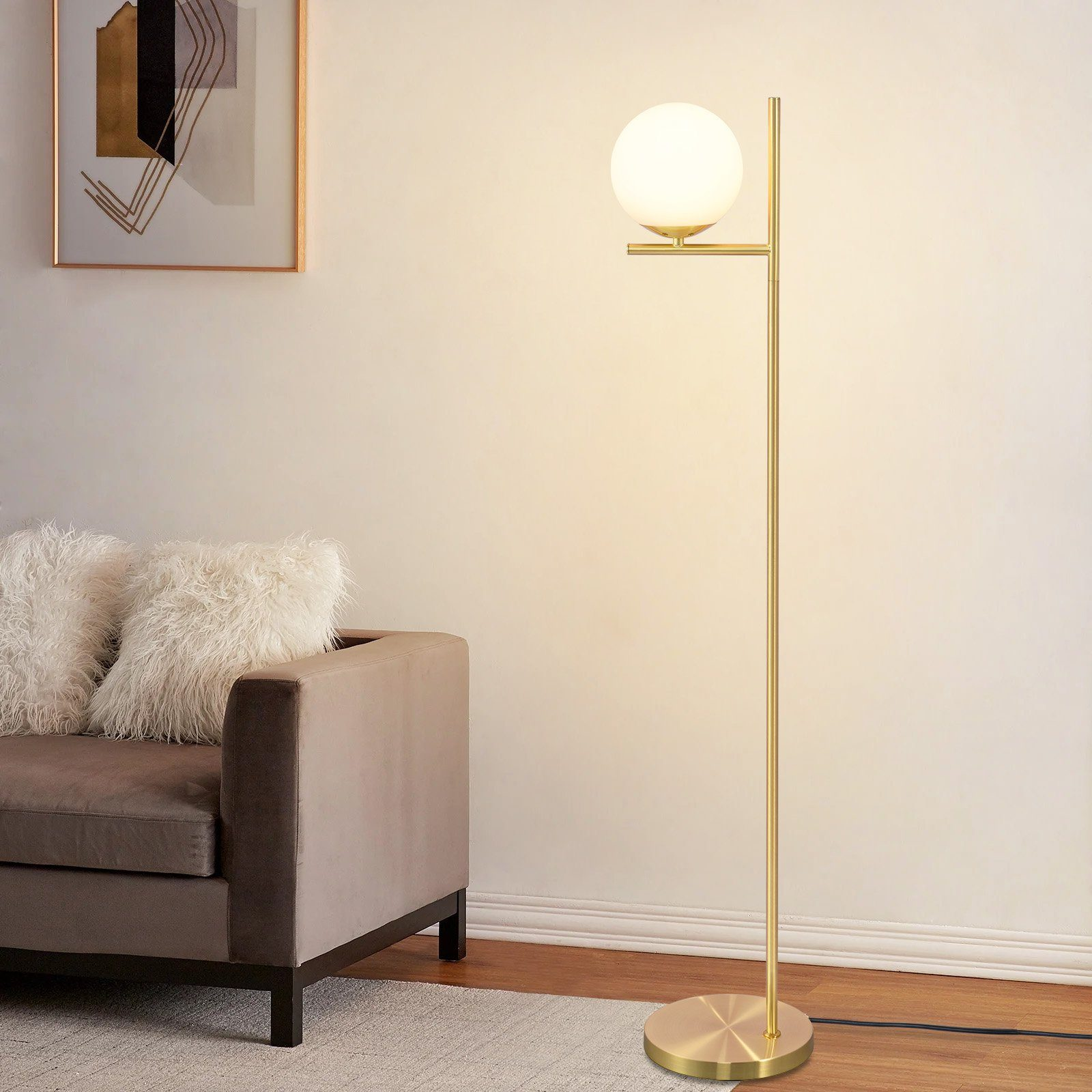 Una lampada da terra dorata con una lampada a globo bianca accanto a un divano marrone e un muro bianco.