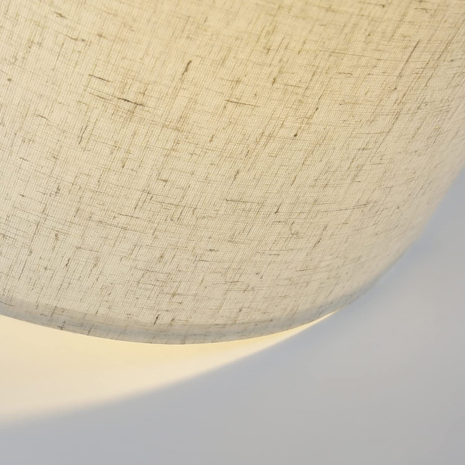 Primo piano di un paralume in tessuto beige chiaro. Il bordo inferiore del paralume si illumina.