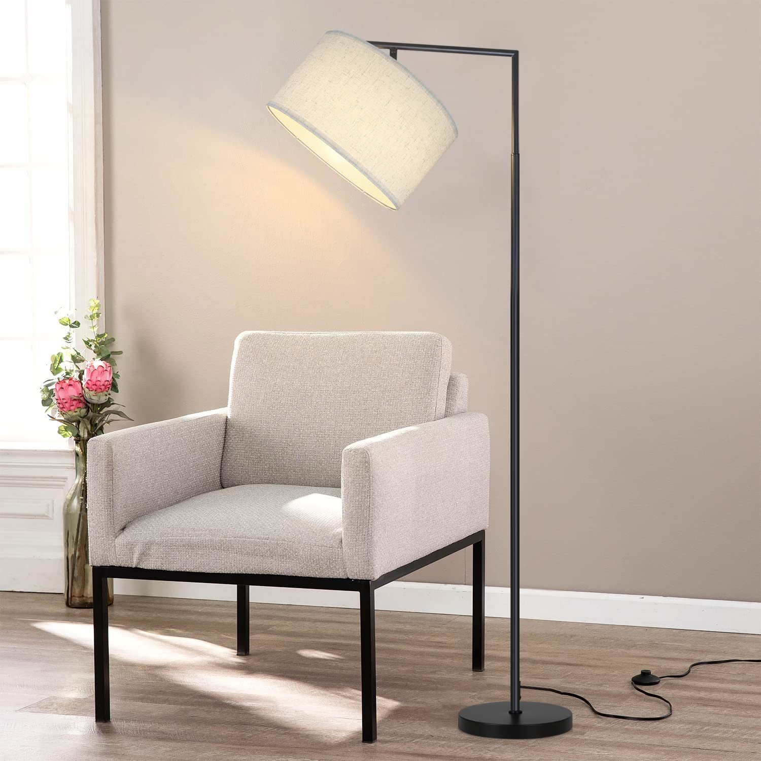 Una lampada da terra nera con un paralume bianco. Una poltrona bianca è accanto alla lampada.