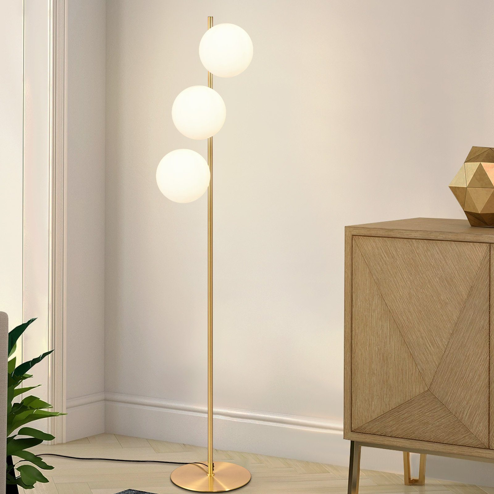 Lampada da terra moderna con tre globi bianchi e base dorata, in un salotto.