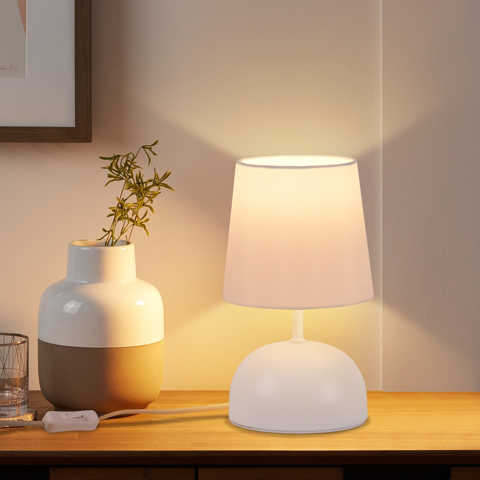 Biała lampa na drewnianym stole obok wazonu z roślinami.