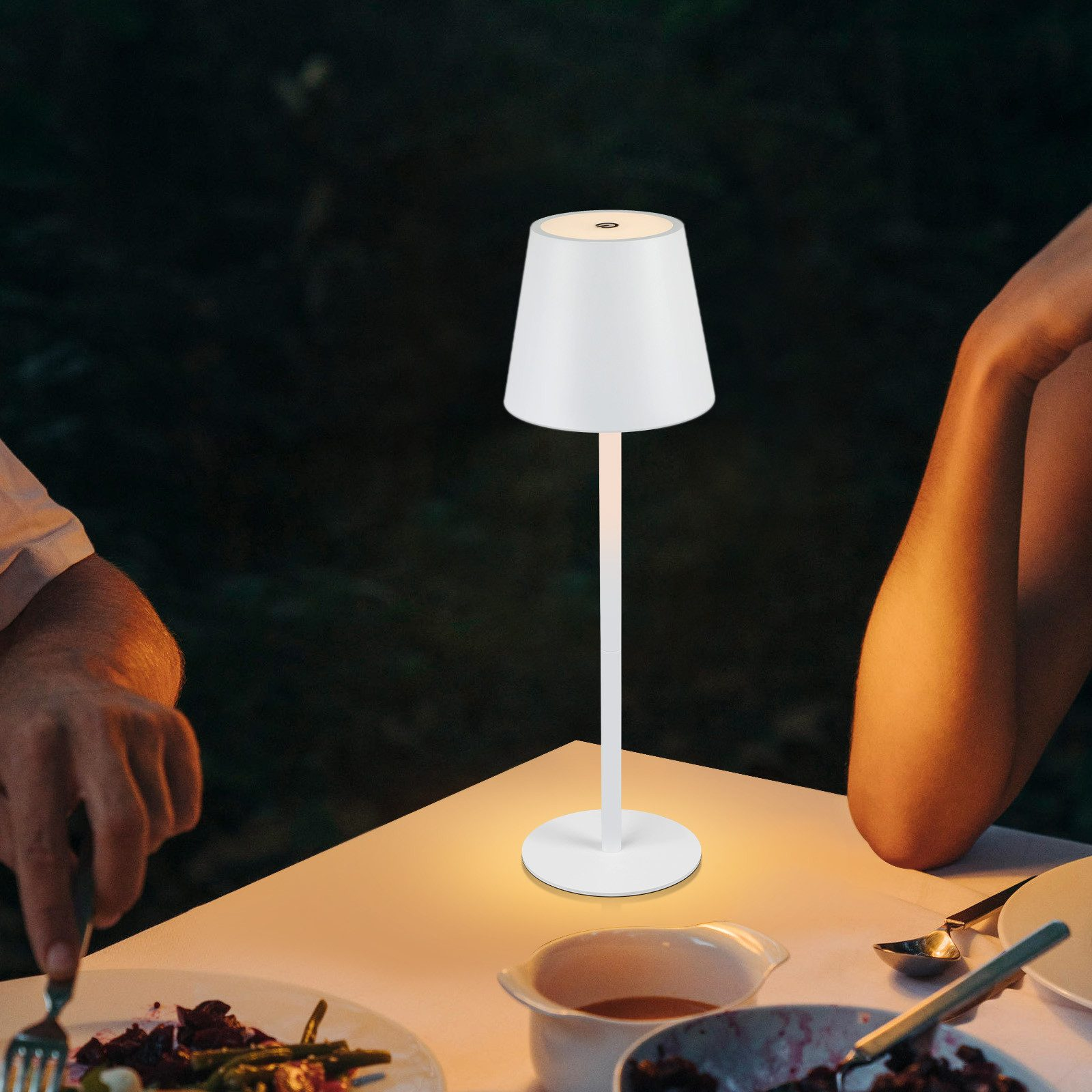 Biała lampa z abażurem stoi na białym stole. Widoczne są dłonie i część ciała.