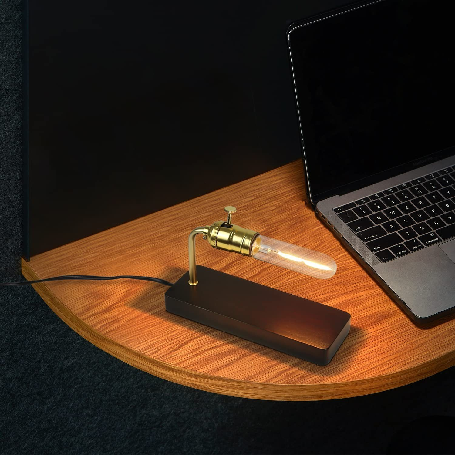 Lampa biurkowa z przezroczystą żarówką i czarną podstawą, na drewnianym stole obok laptopa.