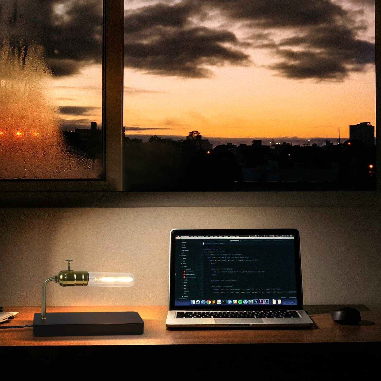 Lampa stołowa, laptop i okno z pomarańczowym niebem.