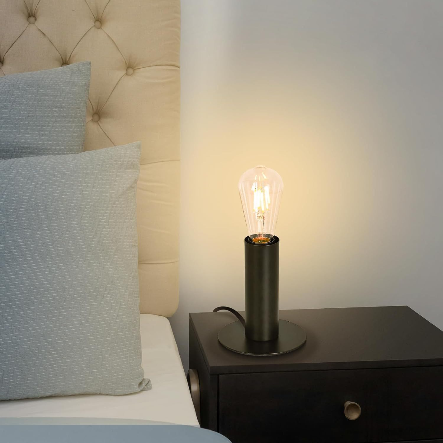 Czarna lampa z żarówką na szafce nocnej obok poduszek i łóżka.