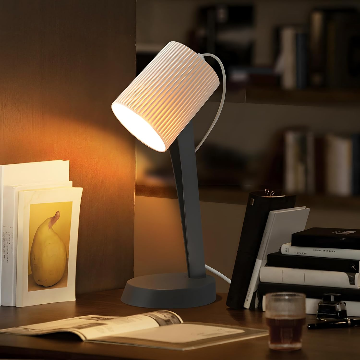 Lampa biurkowa z białym, żebrowanym kloszem, szarą podstawą i książkami na drewnianym biurku.