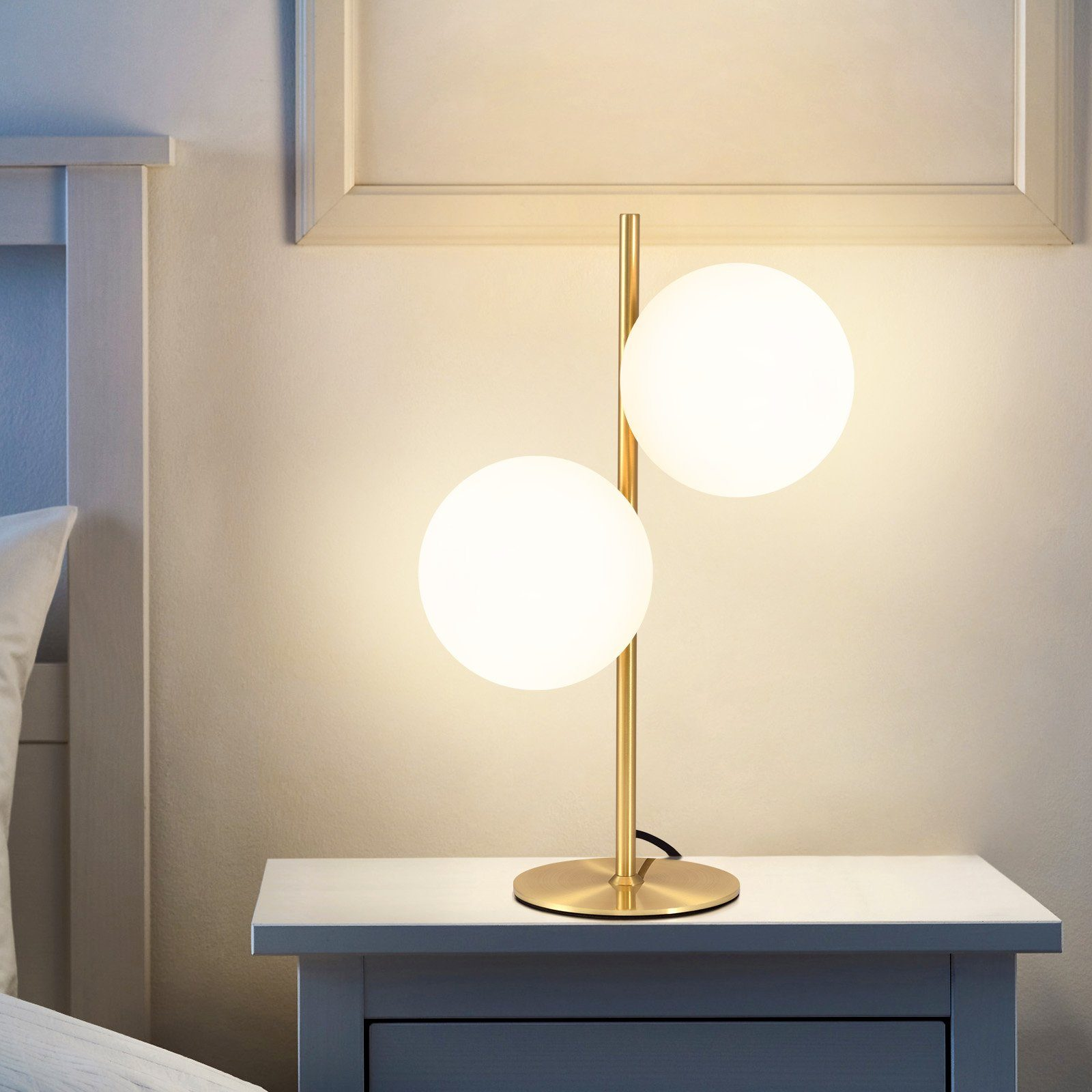 Złota lampa z dwoma białymi kulistymi światłami na białej szafce nocnej.