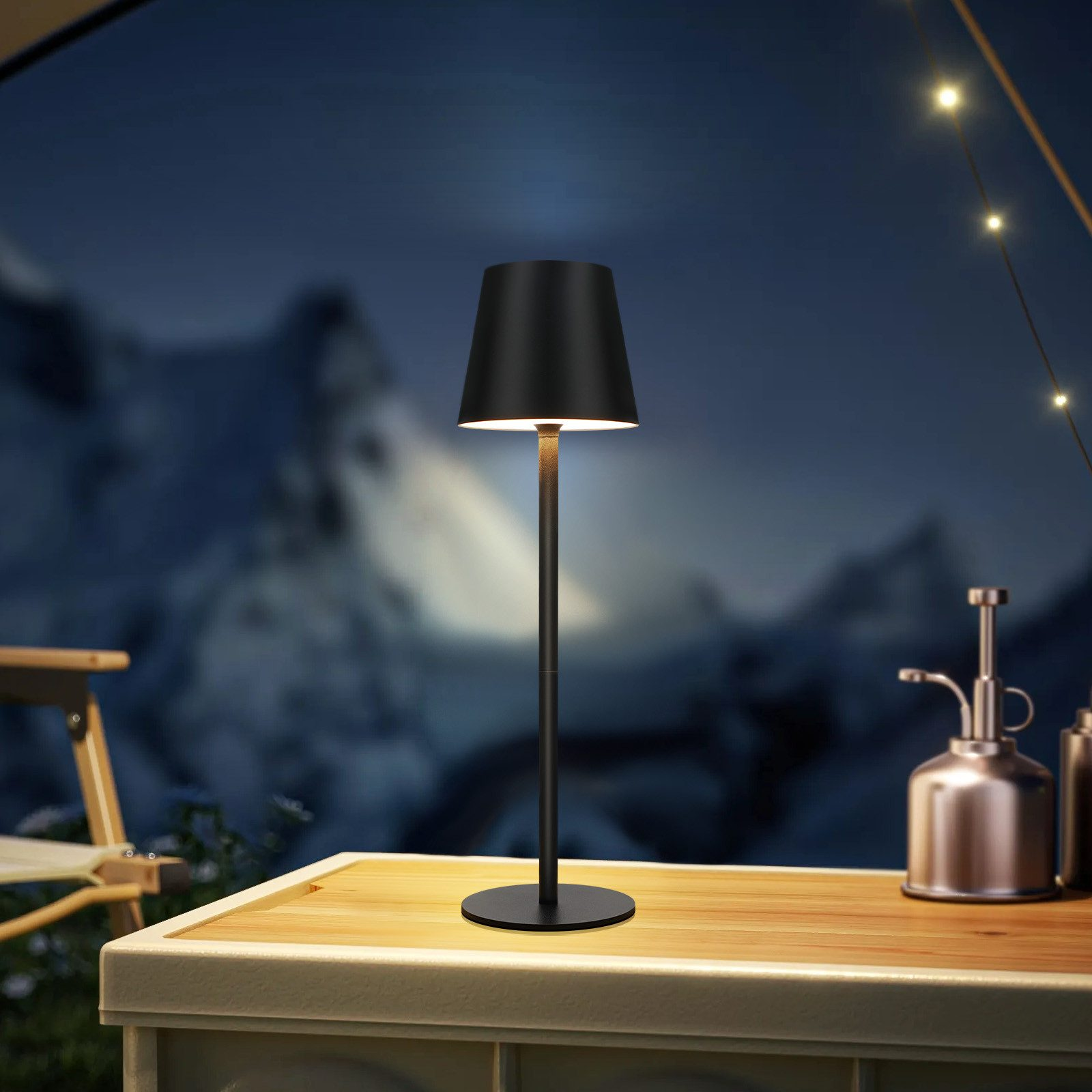 Una lampada nera su un tavolo all'aperto di notte, con una montagna sfocata sullo sfondo.