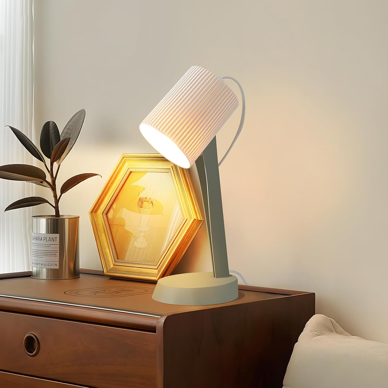 Nowoczesna lampa na stole obok rośliny i obrazu w ramce.