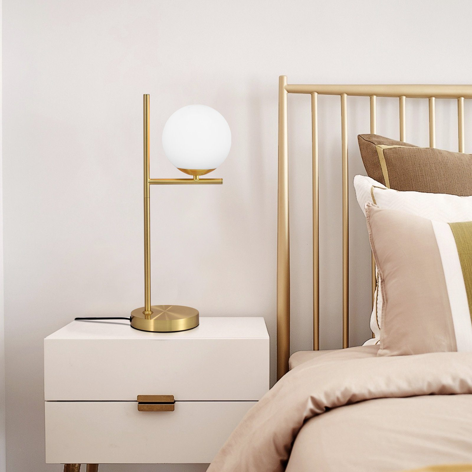 Nowoczesna lampka nocna z białym kloszem w kształcie kuli na złotym stojaku, na białej szafce nocnej.