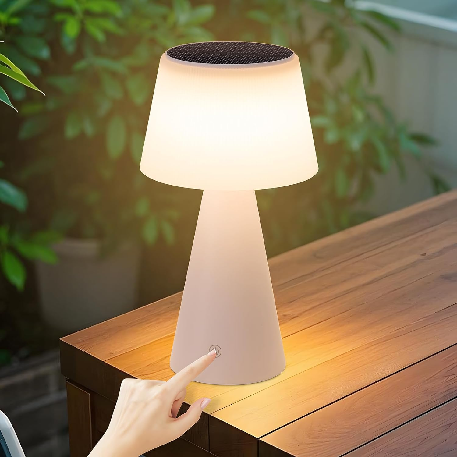 Una lampada bianca con pulsante touch e paralume bianco su un tavolo di legno. Una mano tocca il pulsante.