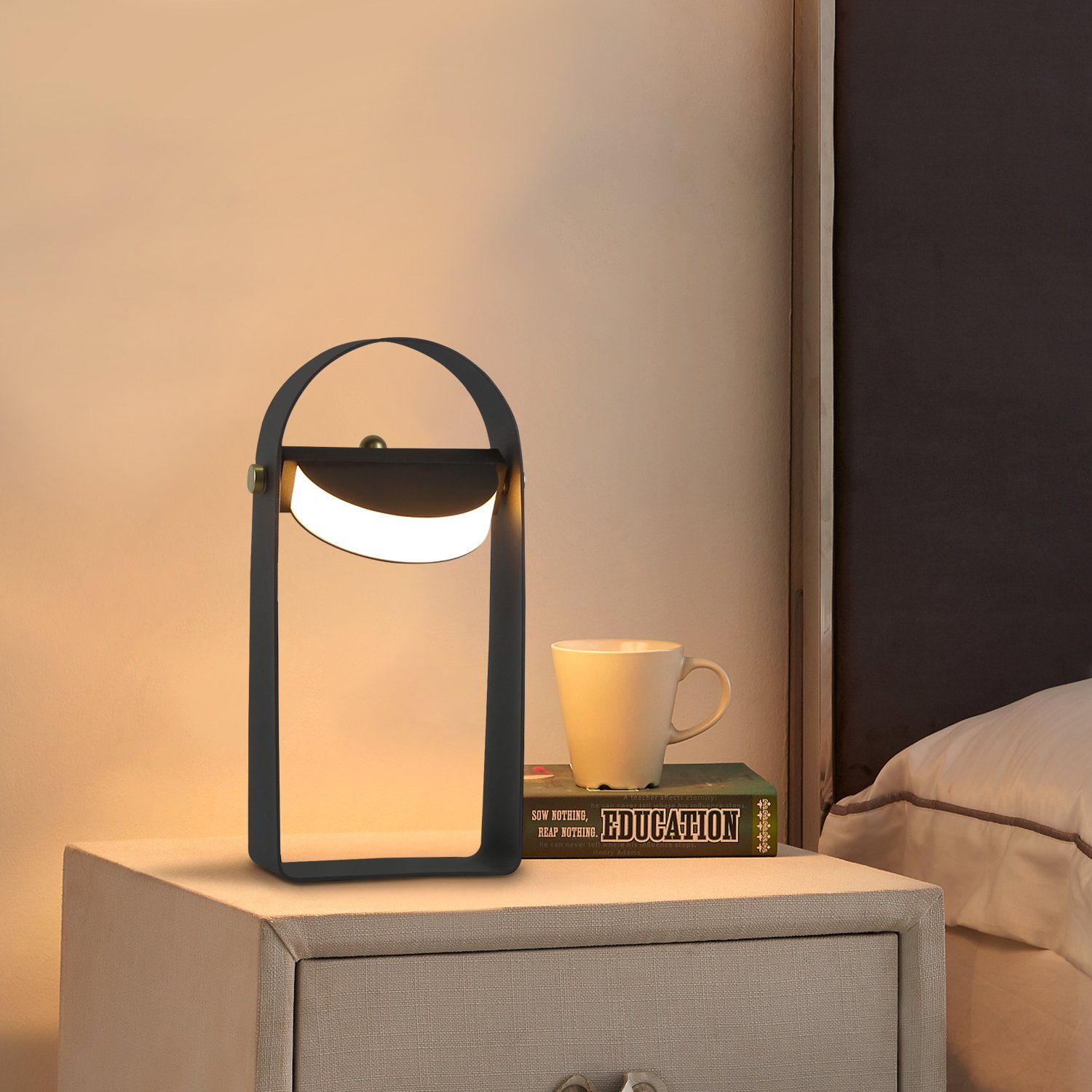 Czarna lampa łukowa na stoliku nocnym z książką i kubkiem. W tle łóżko.