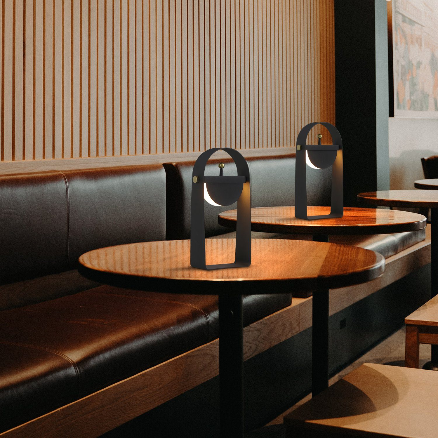 Dwie czarne lampy z łukowatymi ramami, na okrągłych stołach w kawiarni. Ciemnobrązowe siedziska.