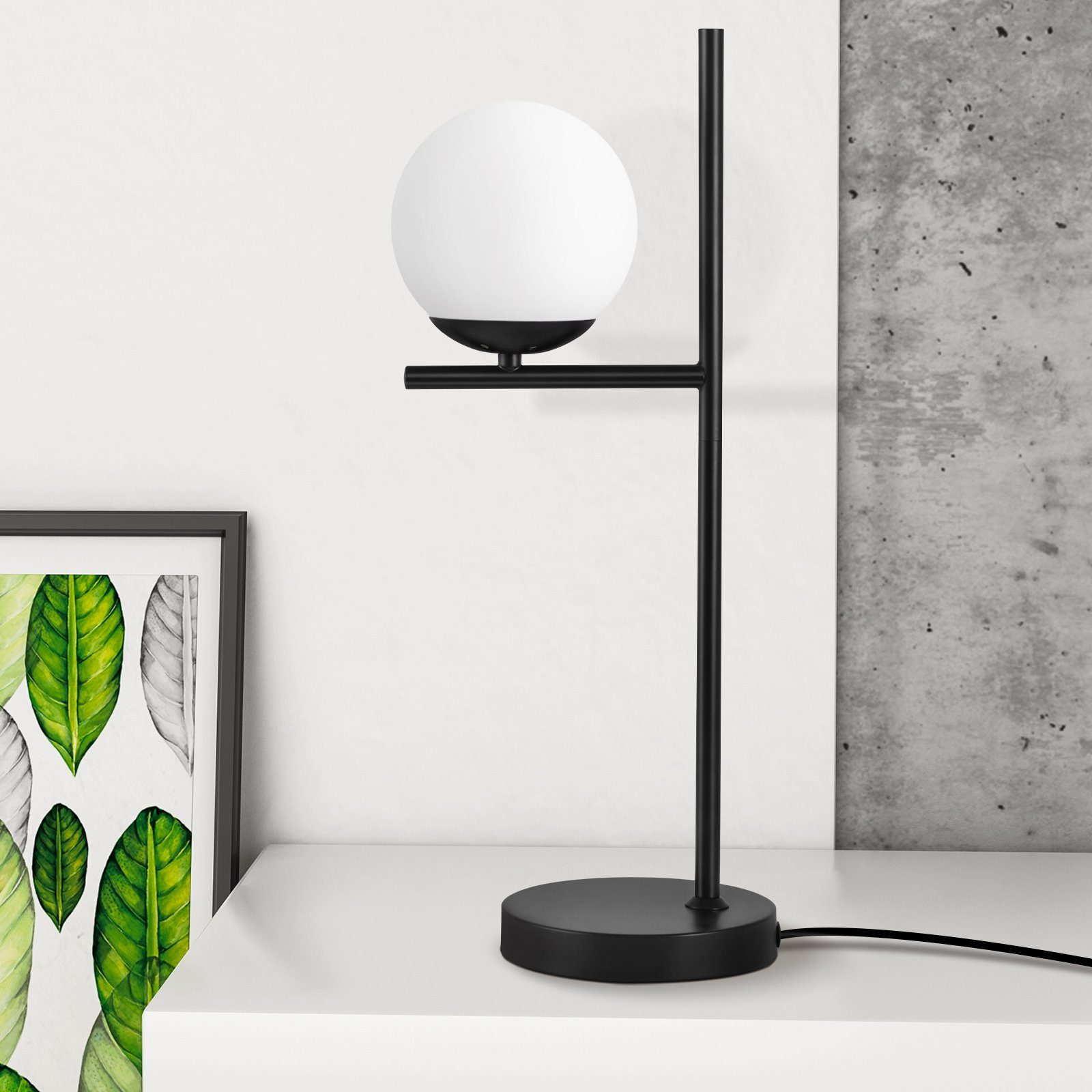 Czarna lampa z białą kulą. Czarna rama z liśćmi i betonowa ściana w tle.