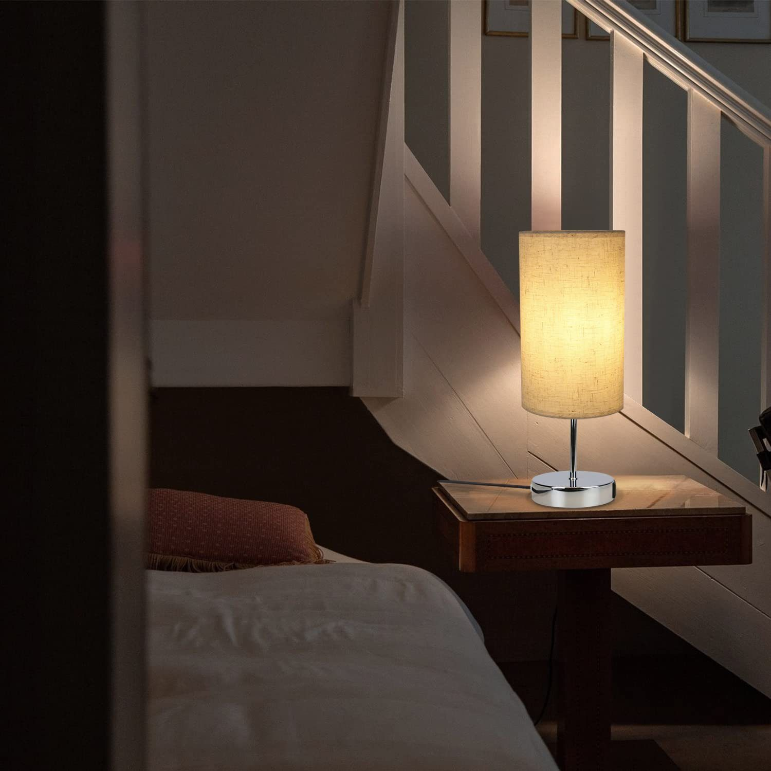 Lampa stołowa z beżowym kloszem, umieszczona na stole w sypialni.