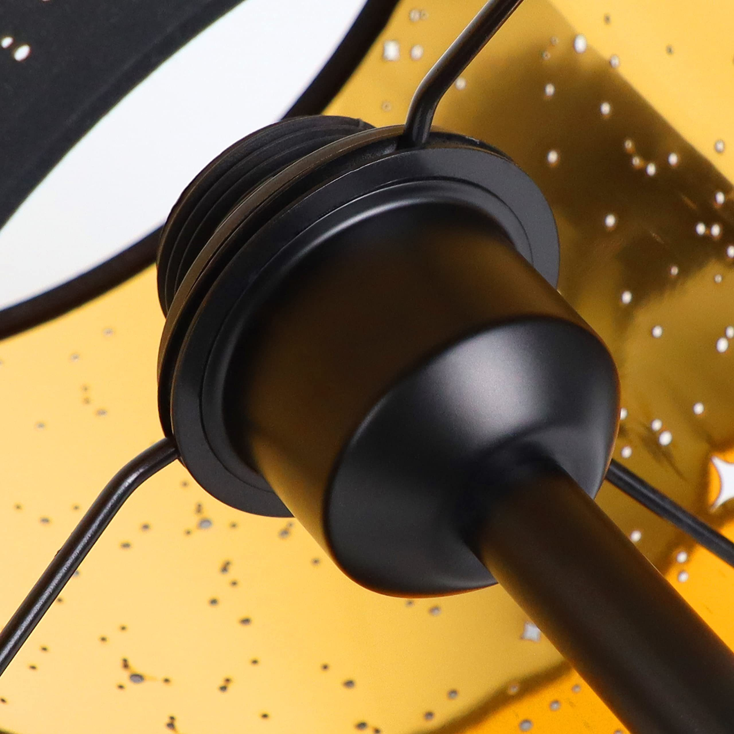 Zbliżenie czarnej podstawy lampy i żółtego klosza z wycięciami w kształcie gwiazd.