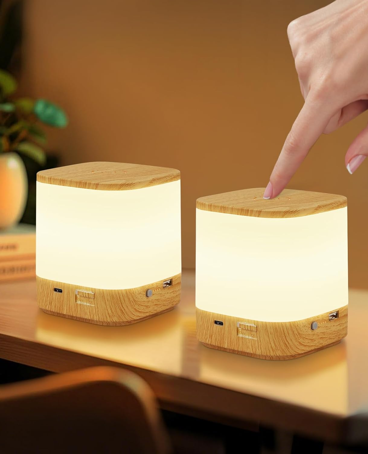 Dwie drewniane lampy na stole. Osoba dotyka palcem wierzchu jednej z lamp.